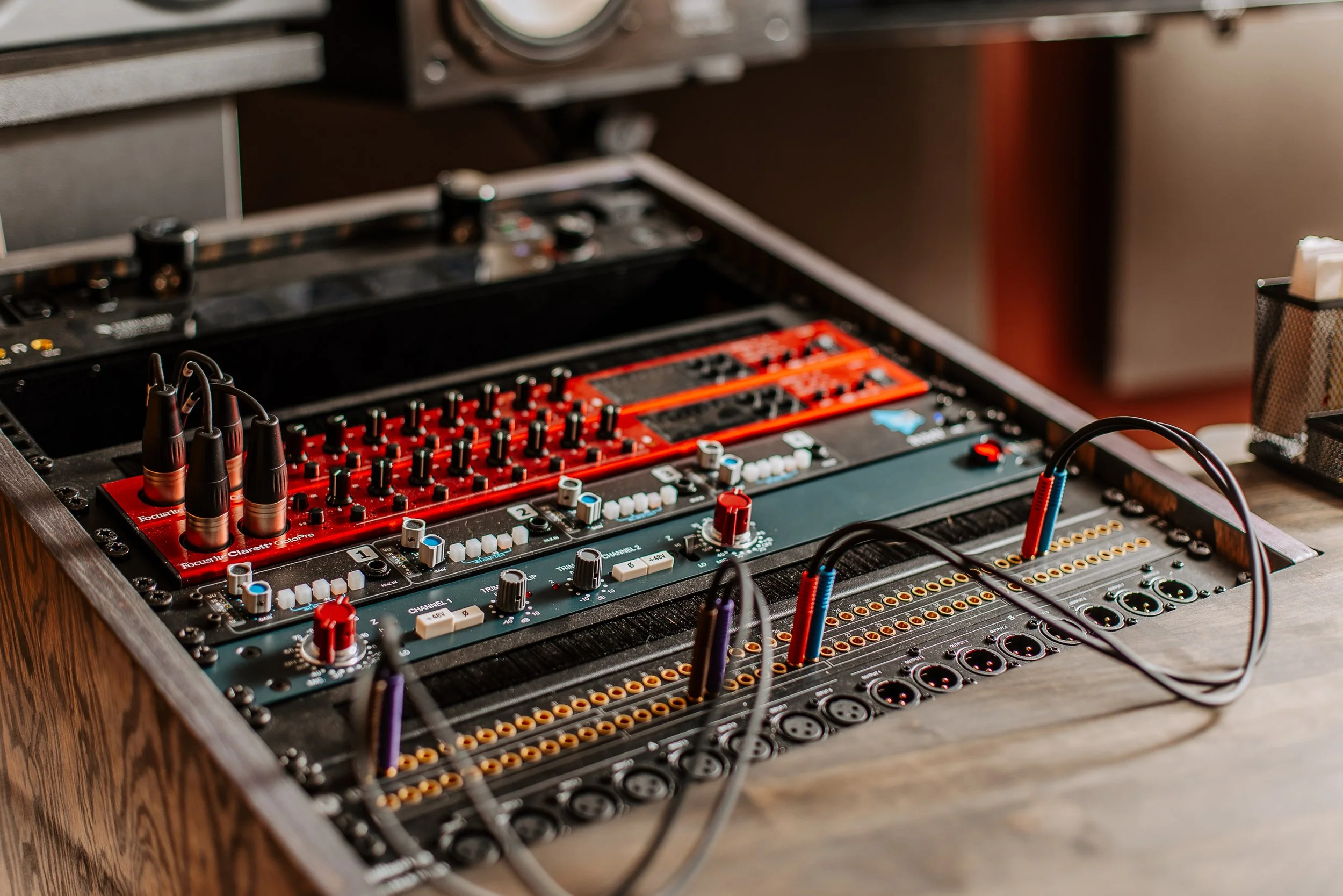Table de mixage audio avec câbles, boutons, et contrôleurs, située sur un banc en bois.