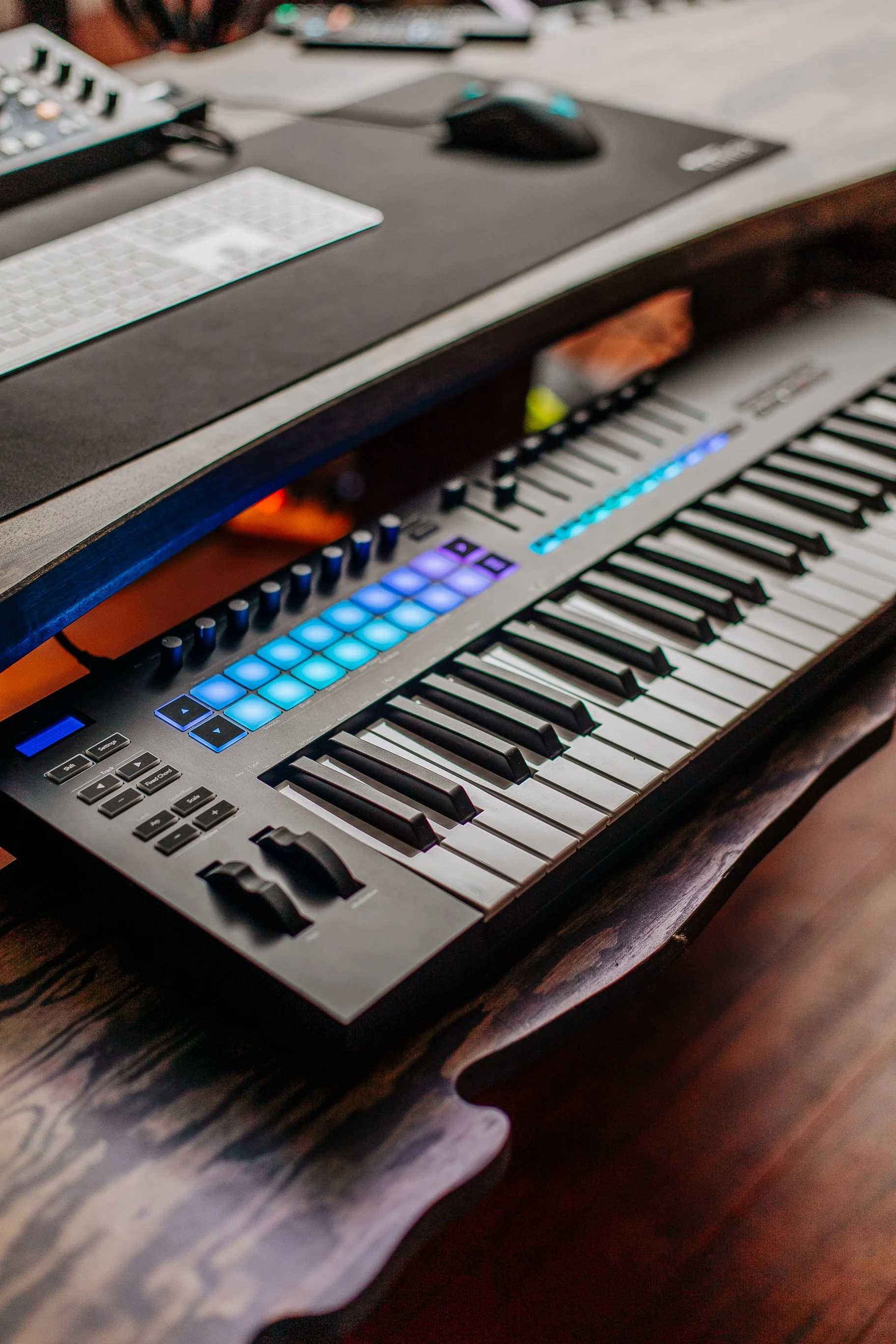 Clavier de piano numérique avec des boutons de contrôle lumineux, placé sur un bureau en bois, avec un ordinateur portable et une souris au-dessus.