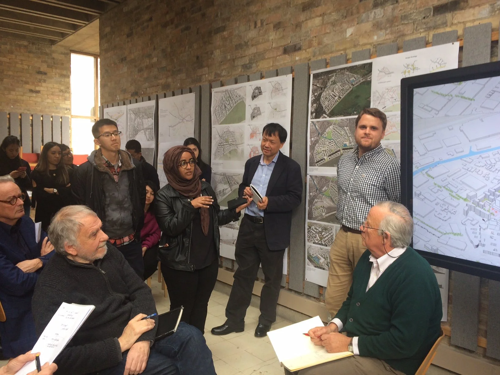 Sabrina Hussein presenting with Ying Jin, Sjoerd Soeters, Peter Buchanan listening.