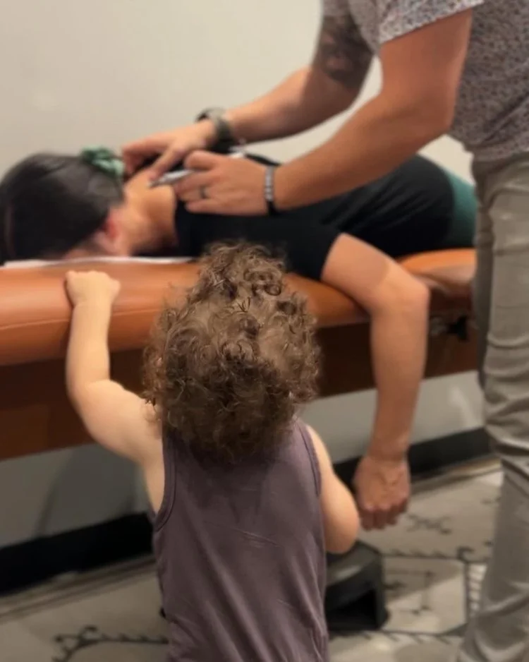 Child watches as a parent receives a gentle Torque Release chiropractic adjustment in Cypress, TX