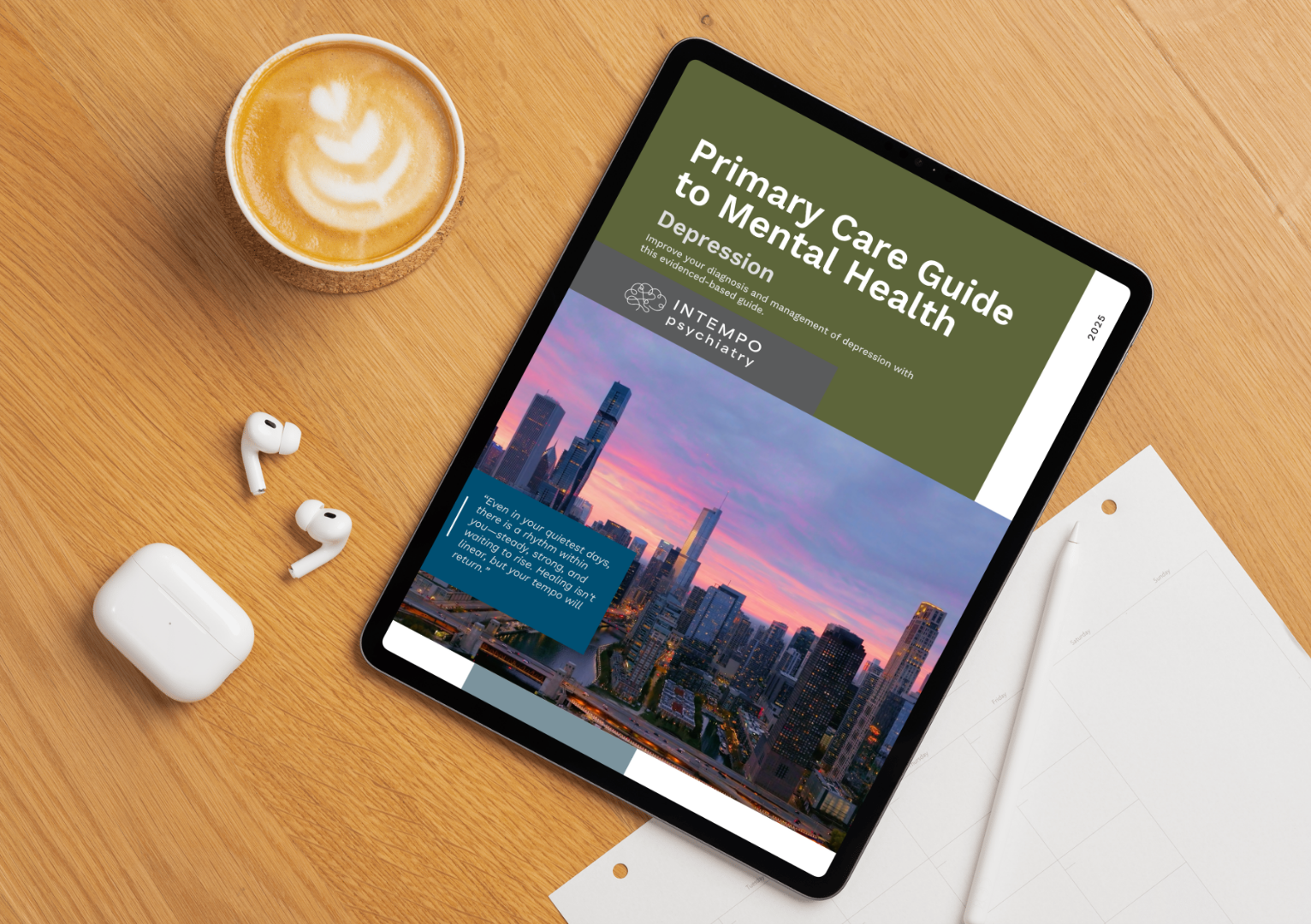 Tablet displaying a guide titled 'Primary Care Guide to Mental Health Depression' on a wooden desk, with wireless earbuds, a white charging case, a cup of coffee with latte art, a white pen, and a white notebook nearby.