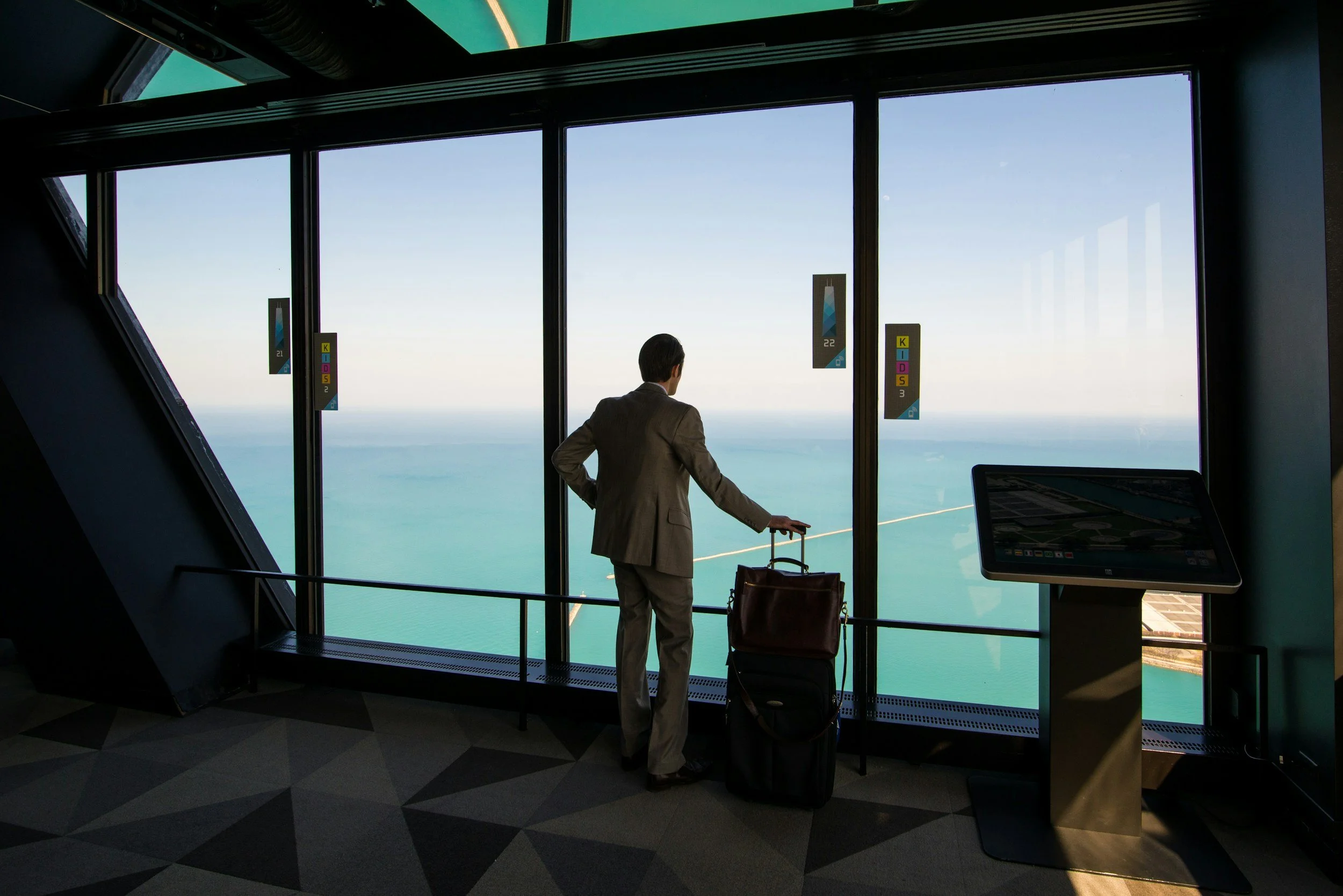 Un homme d'affaires regarde par les grandes vitres de l'aéroport avec vue vers l'océan