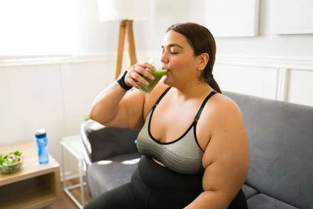 Healthy woman drinking a green juice before exercising as part of her weight loss plan