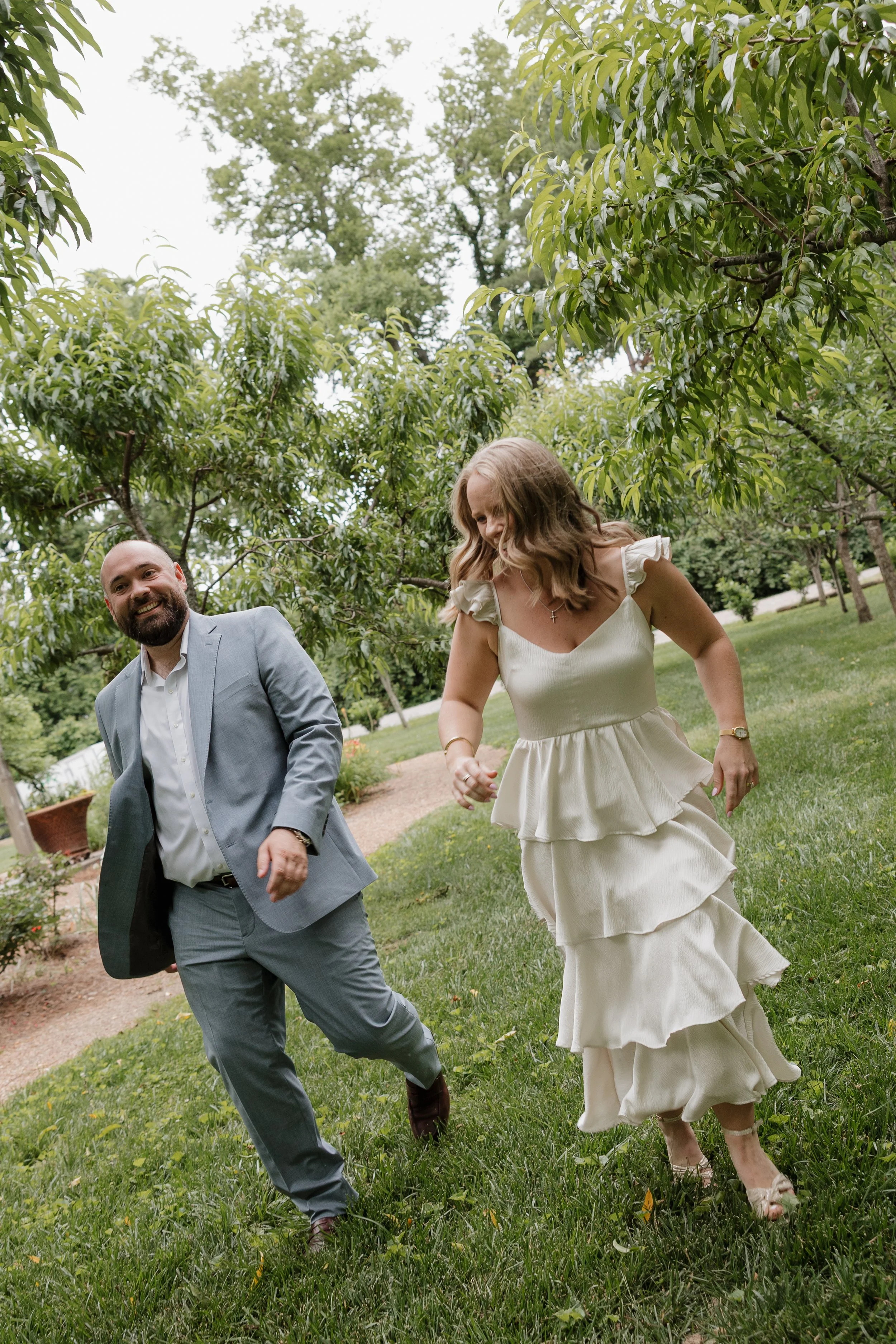 Candid Washington DC Engagement Photos A man and woman are running and laughing outdoors in a lush green park or garden.