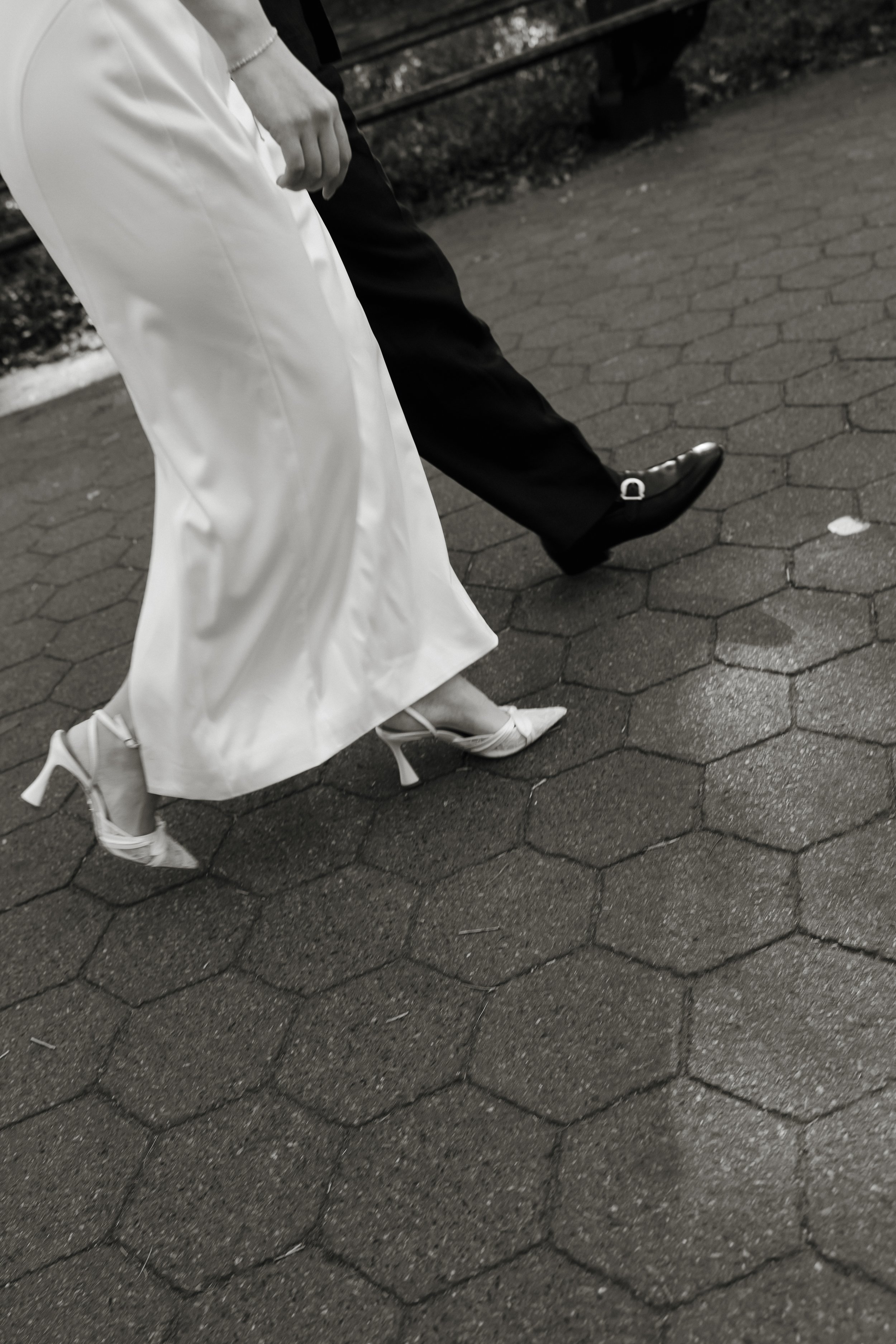 Lovers walking on a brick sidewalk, dressed in formal attire, holding hands, black and white photo. DC Wedding Photographer. Michaela Mae and Co.