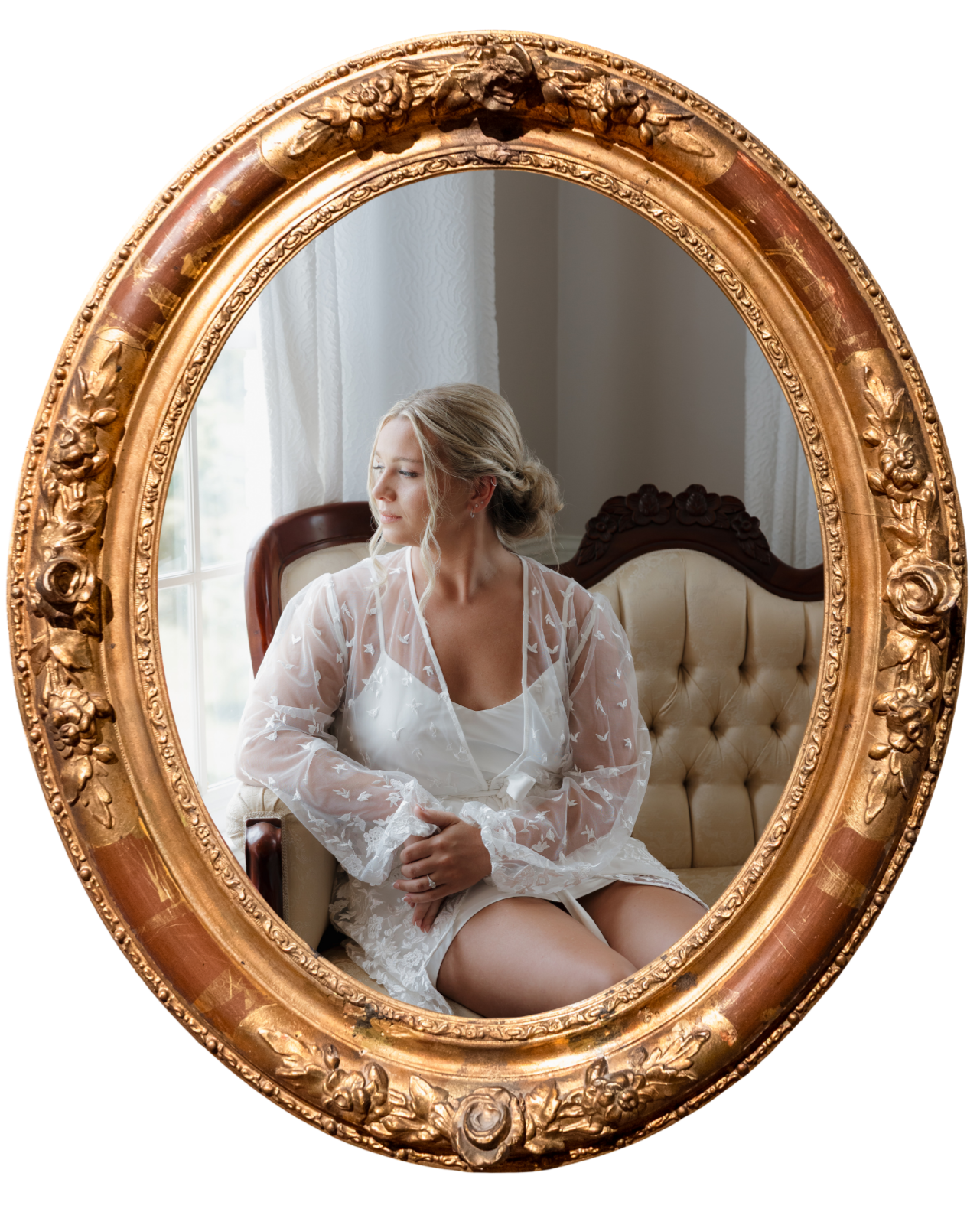 DC Wedding Photographer  A woman in white clothing sitting on a vintage sofa, looking out a window, seen through an ornate gold-framed mirror.