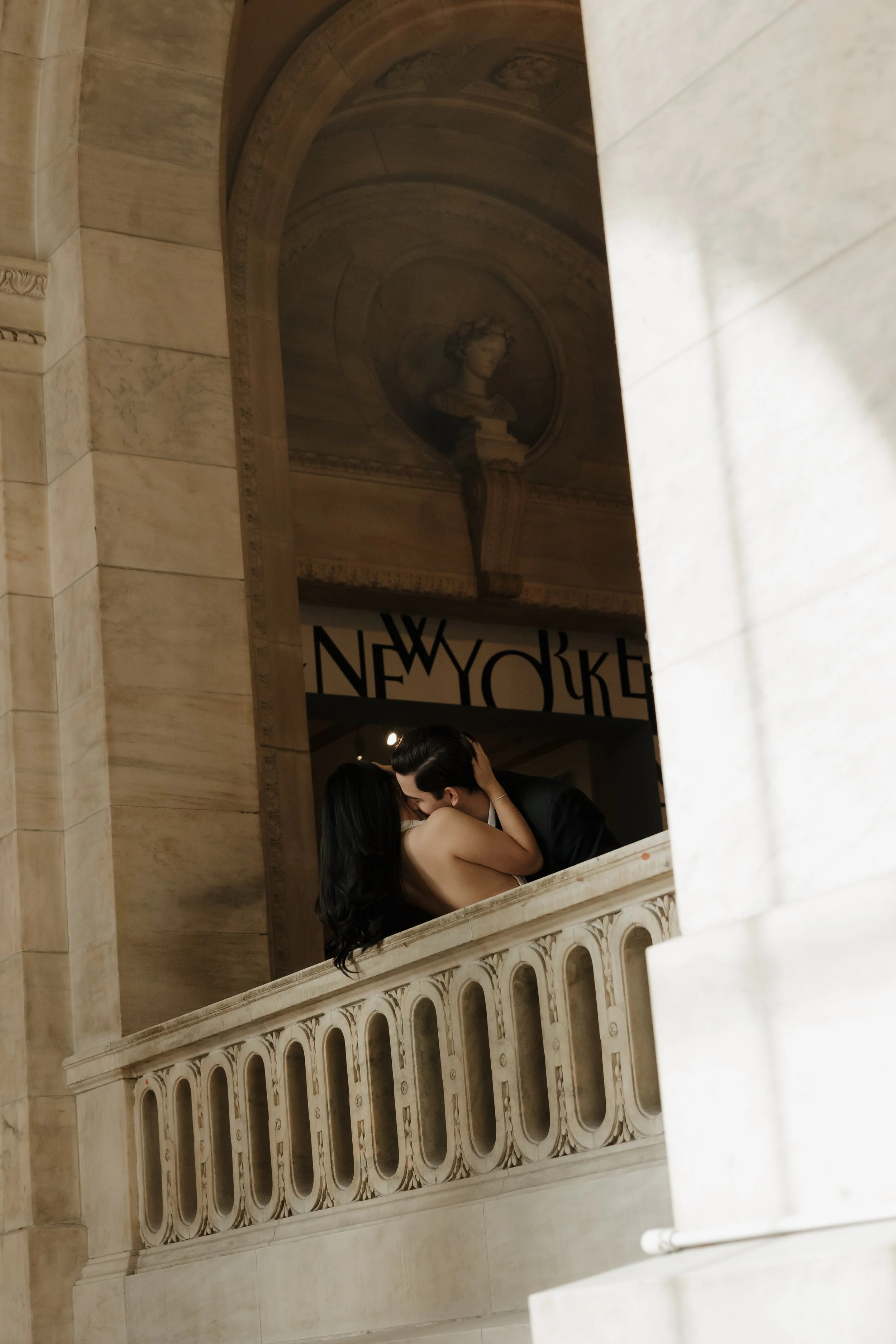 DC Wedding Photographer. A couple kissing on a balcony inside a building with marble architecture and a painted bust sculpture in a niche above.