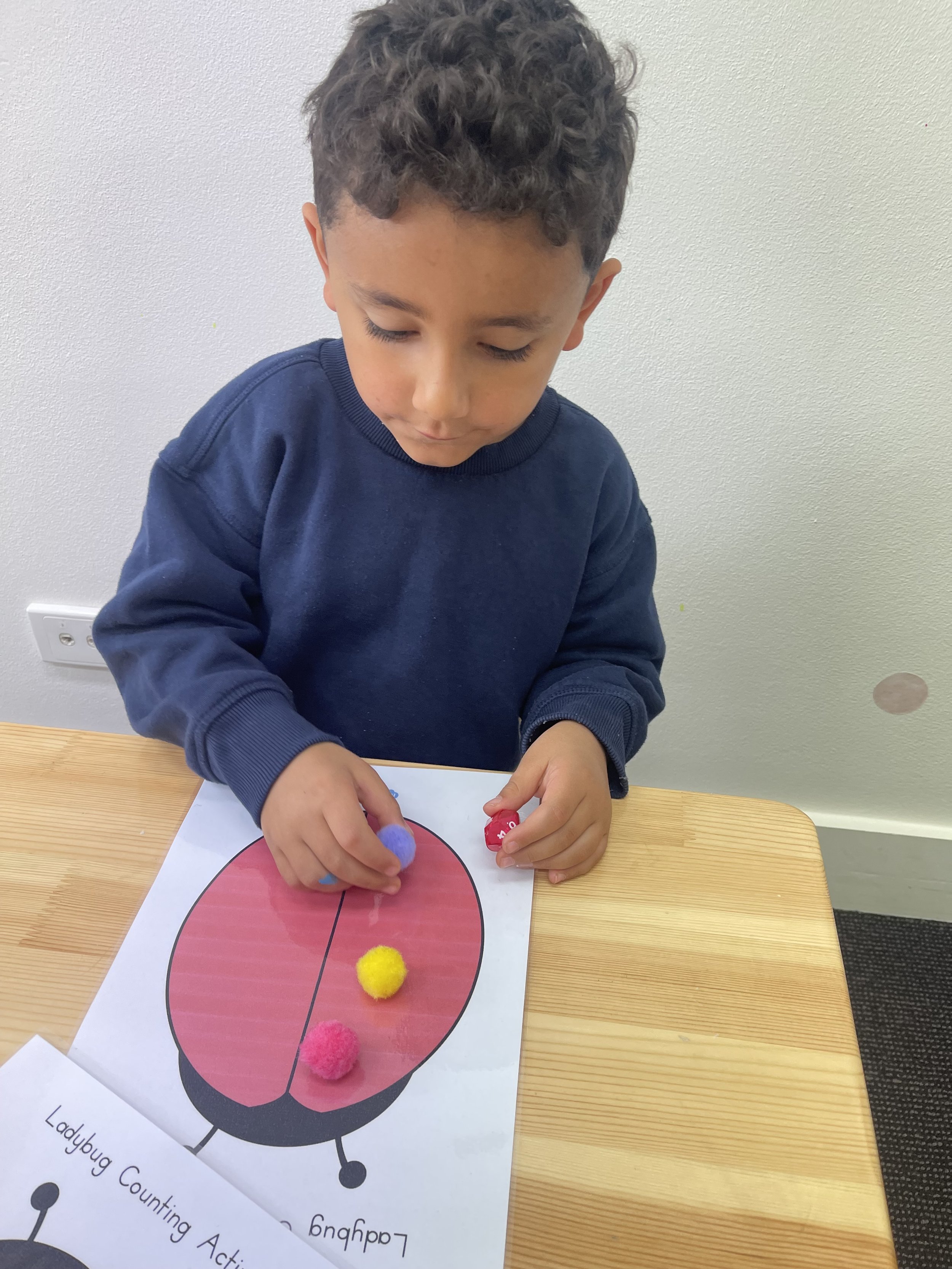 A young girl with curly red hair, wearing a pink sweater, playing with colorful stacking rings on a white table.