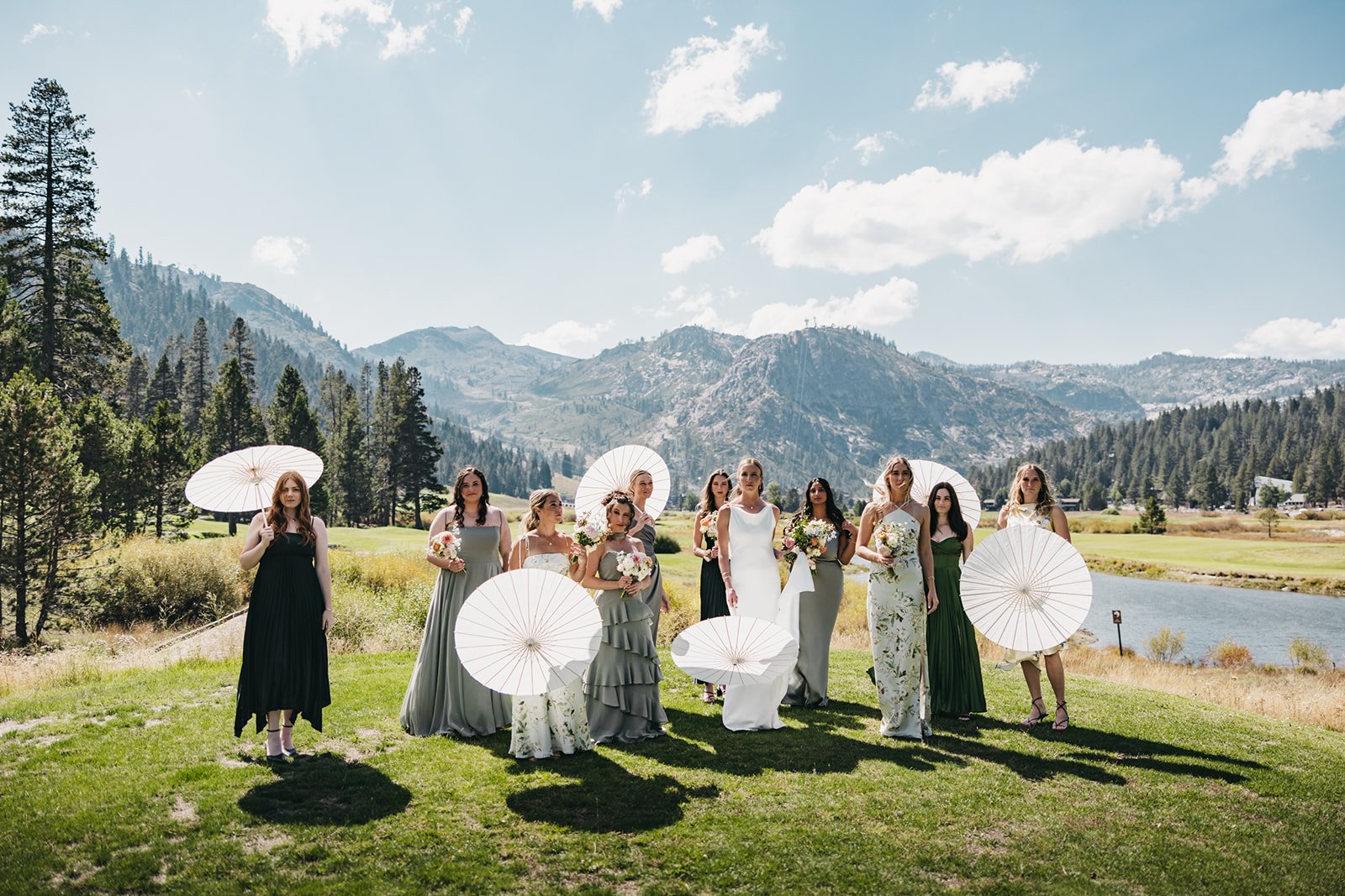 A wedding party walking outdoors in a scenic mountain landscape at Everline Resort. The group includes the bride, wearing a white wedding dress, and several bridesmaids in various pastel and floral dresses.