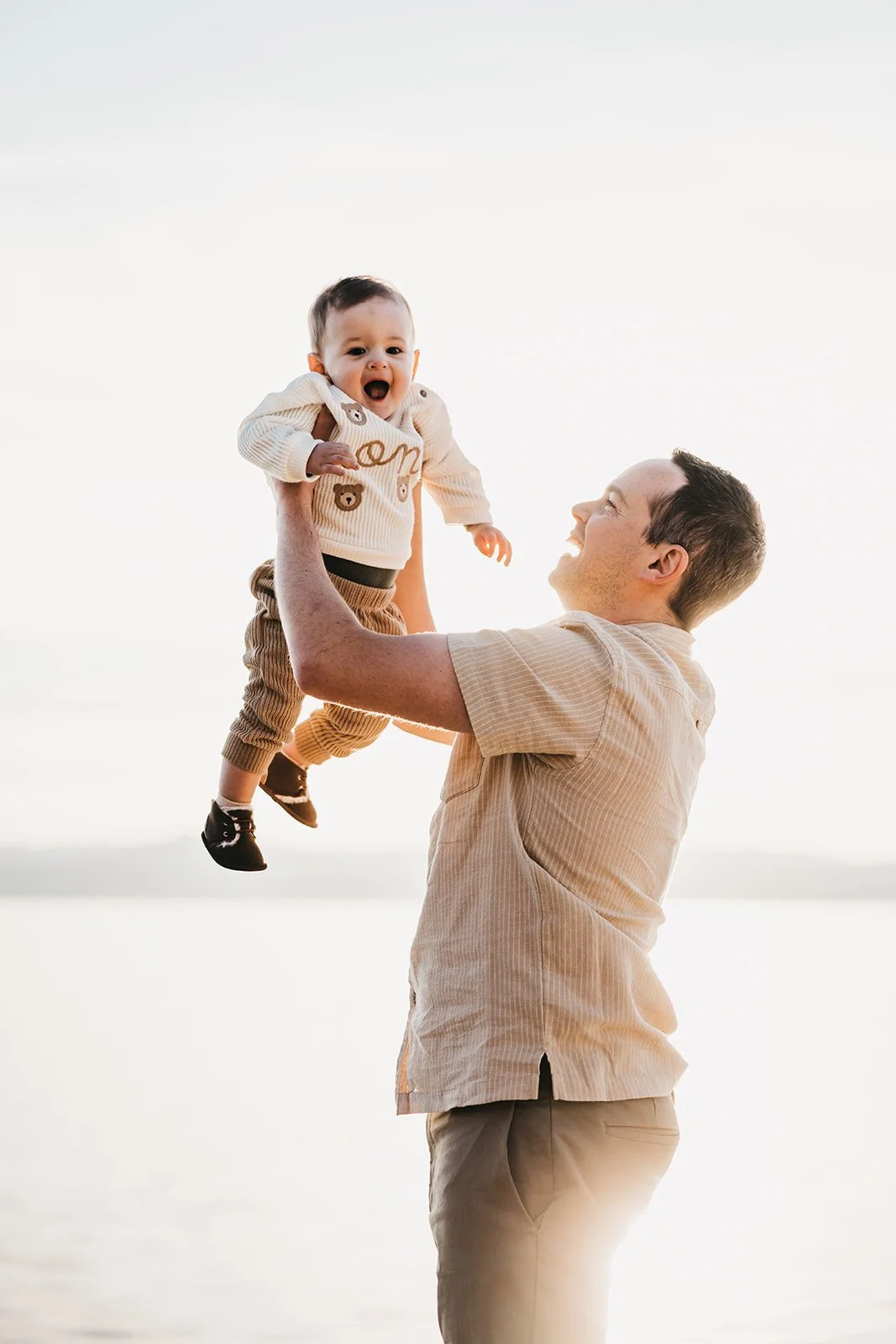 A man lifting a laughing baby in the air outdoors during sunset.