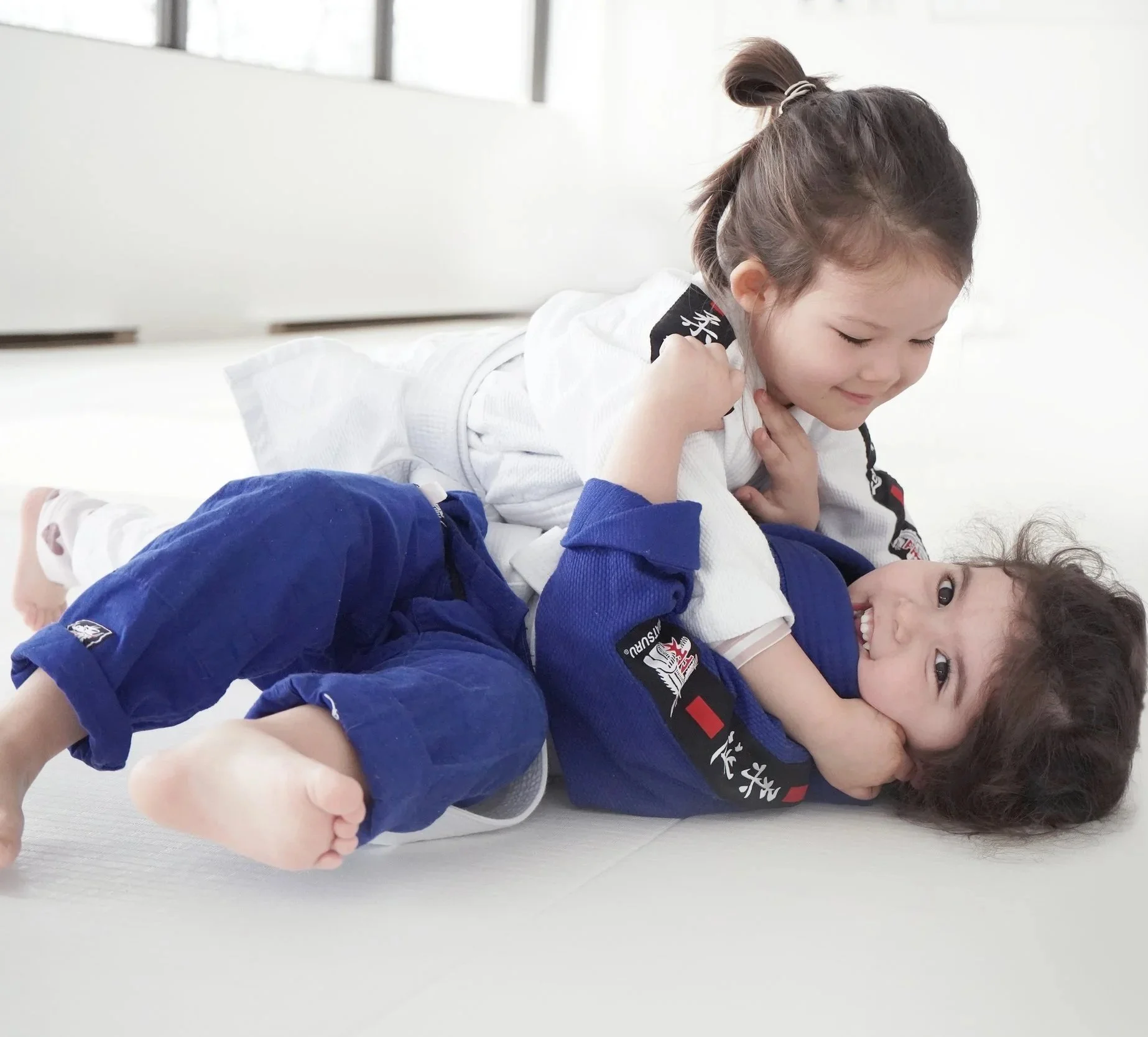 Deux personnes pratiquent des arts martiaux dans une salle lumineuse, portant des vêtements de sport noirs et bleus.