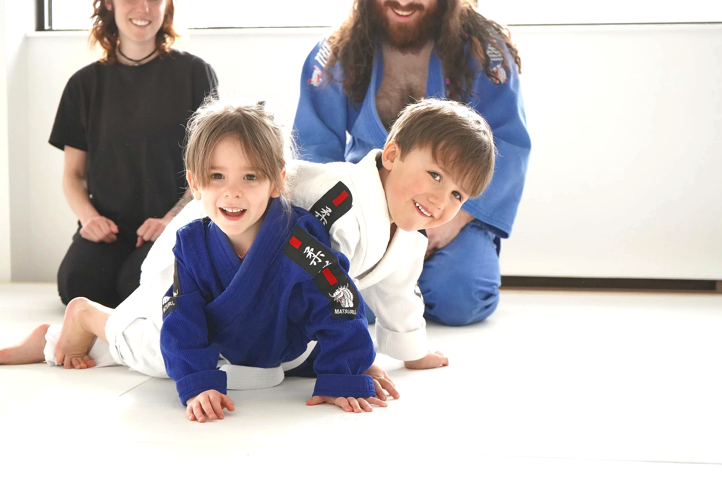 Jeune enfant en kimono de judo blanc avec ceinture, souriant, contre un fond blanc.