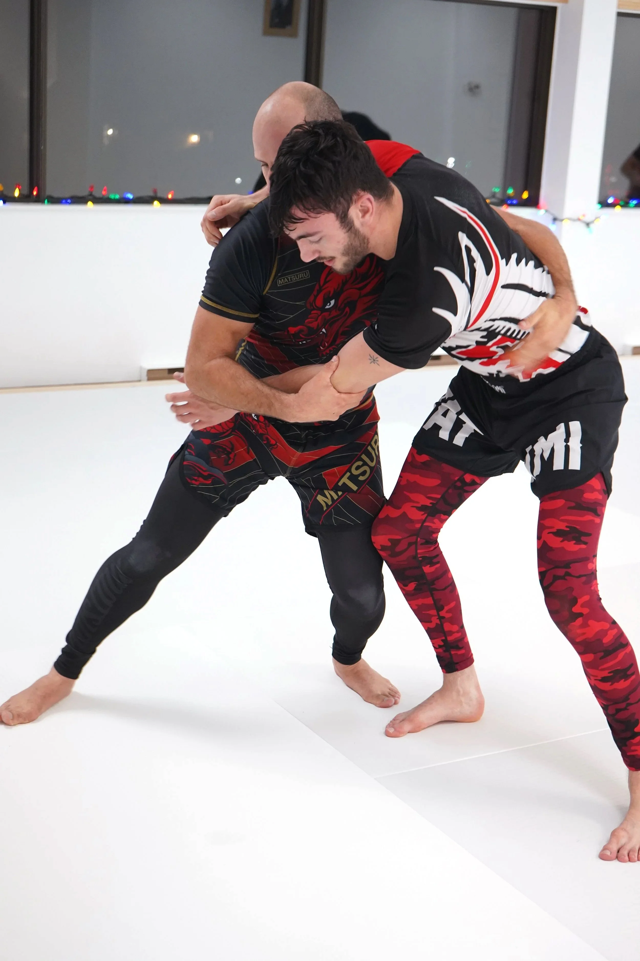 Des personnes pratiquant des arts martiaux dans une salle d'entraînement, par petits groupes, pieds nus sur un tatami blanc.
