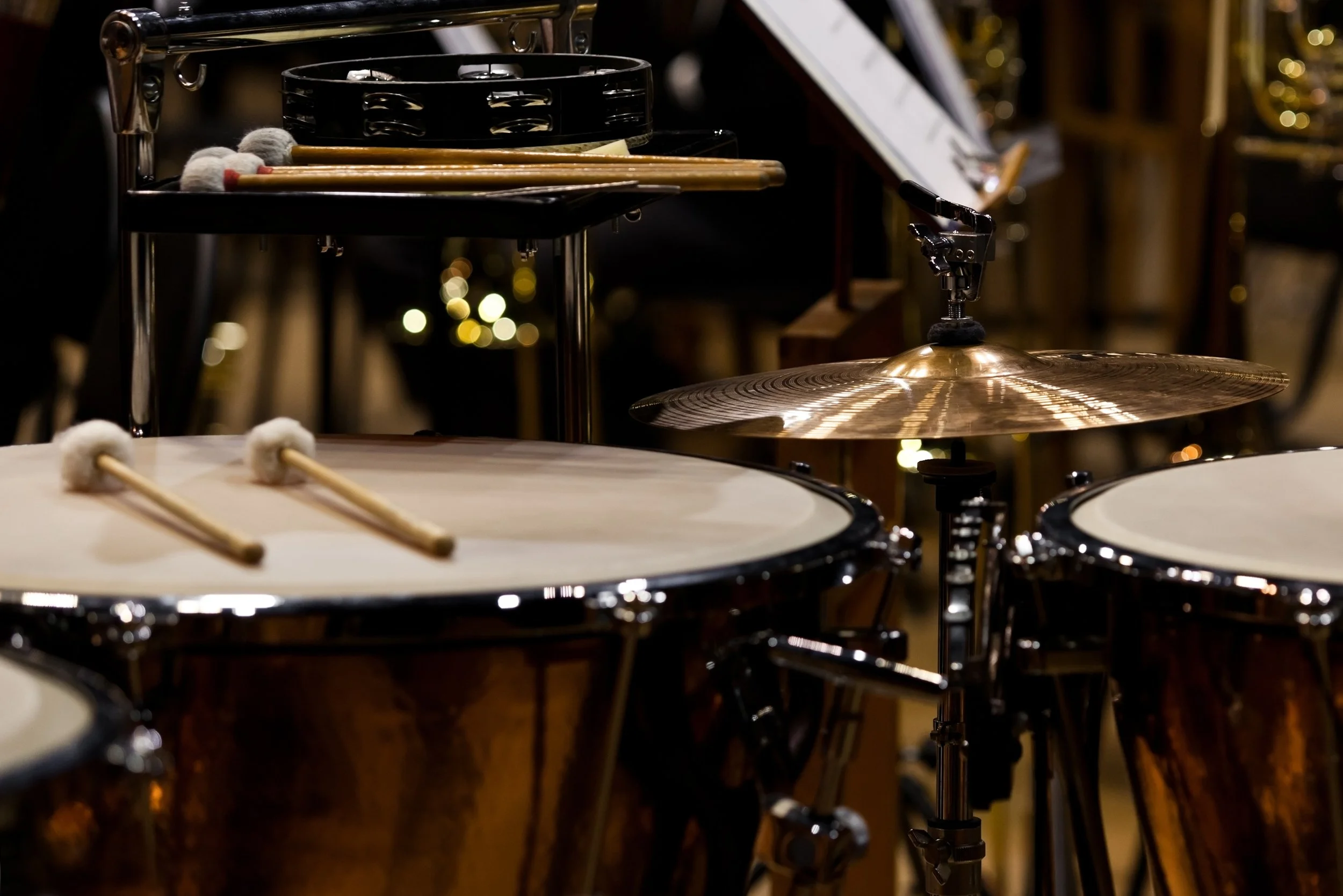 A multi-percussion set-up, featuring a suspended cymbal, two timpani, a black rock tambourine, and mallets.