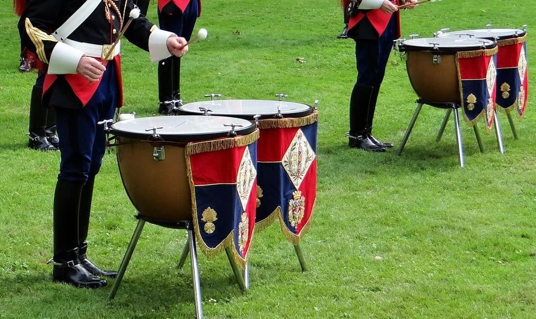 Two pairs of marching timpani on a grassy field. The drums don't have pedals and are instead tunable via hand cranks on each lug around the head.