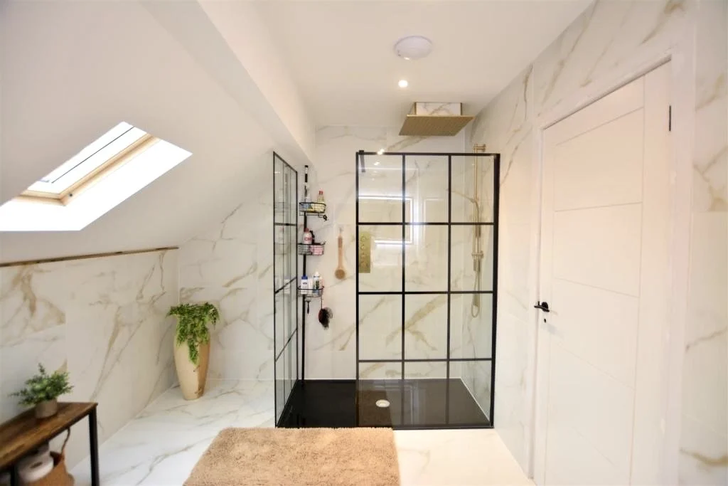 Modern bathroom with marble walls, a glass-enclosed shower, skylight, and white door.