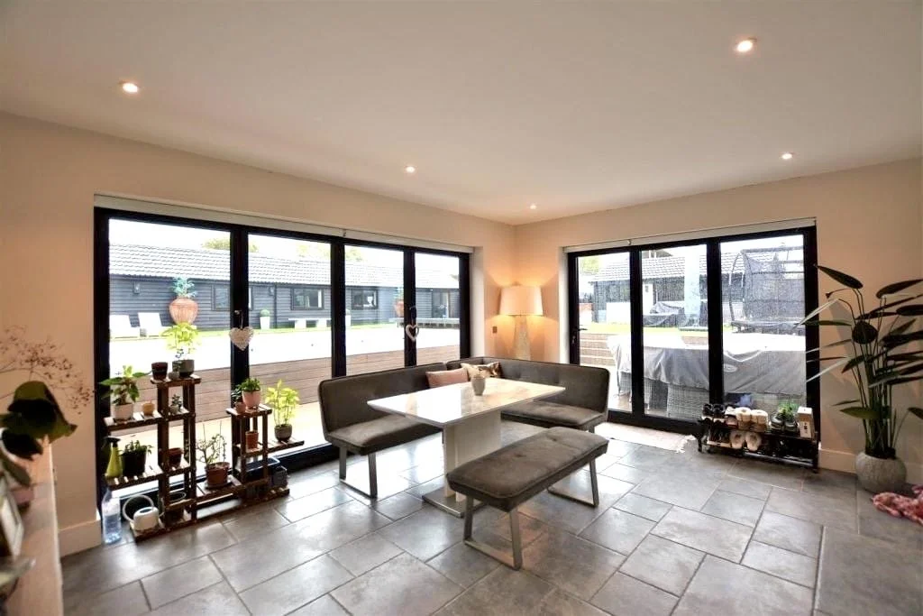 Living room with large sliding glass doors, gray dining table with bench and chairs, potted plants, and indoor lighting.