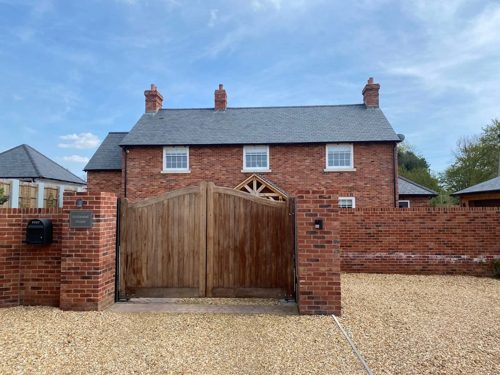 A brick house with a wooden gate, surrounded by a brick wall, under a blue sky with some clouds.