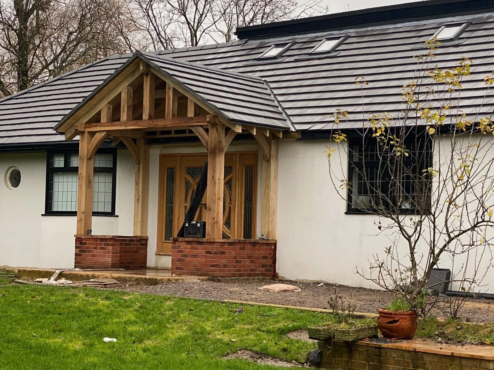 Front view of a house under construction or renovation, with a new wooden porch framing, brick steps, and a shingled roof with skylights