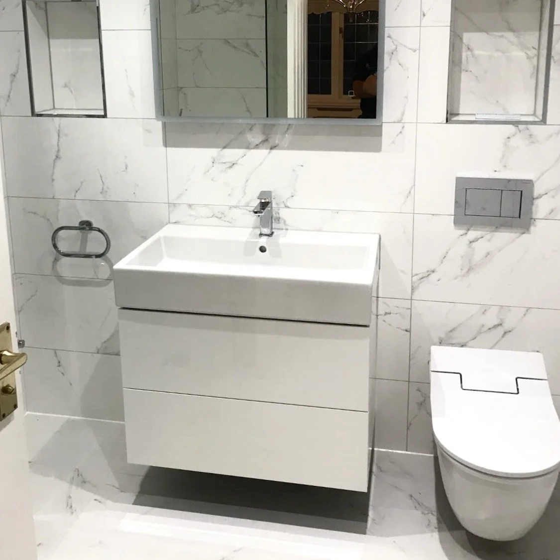 Modern bathroom with a white sink vanity, wall-mounted mirror, toilet, and marble wall tiles.