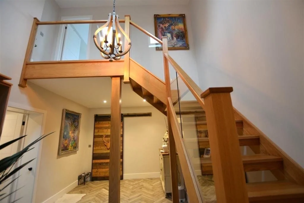 Interior view of a two-story home with a wooden staircase, chandelier, and artwork on the walls.