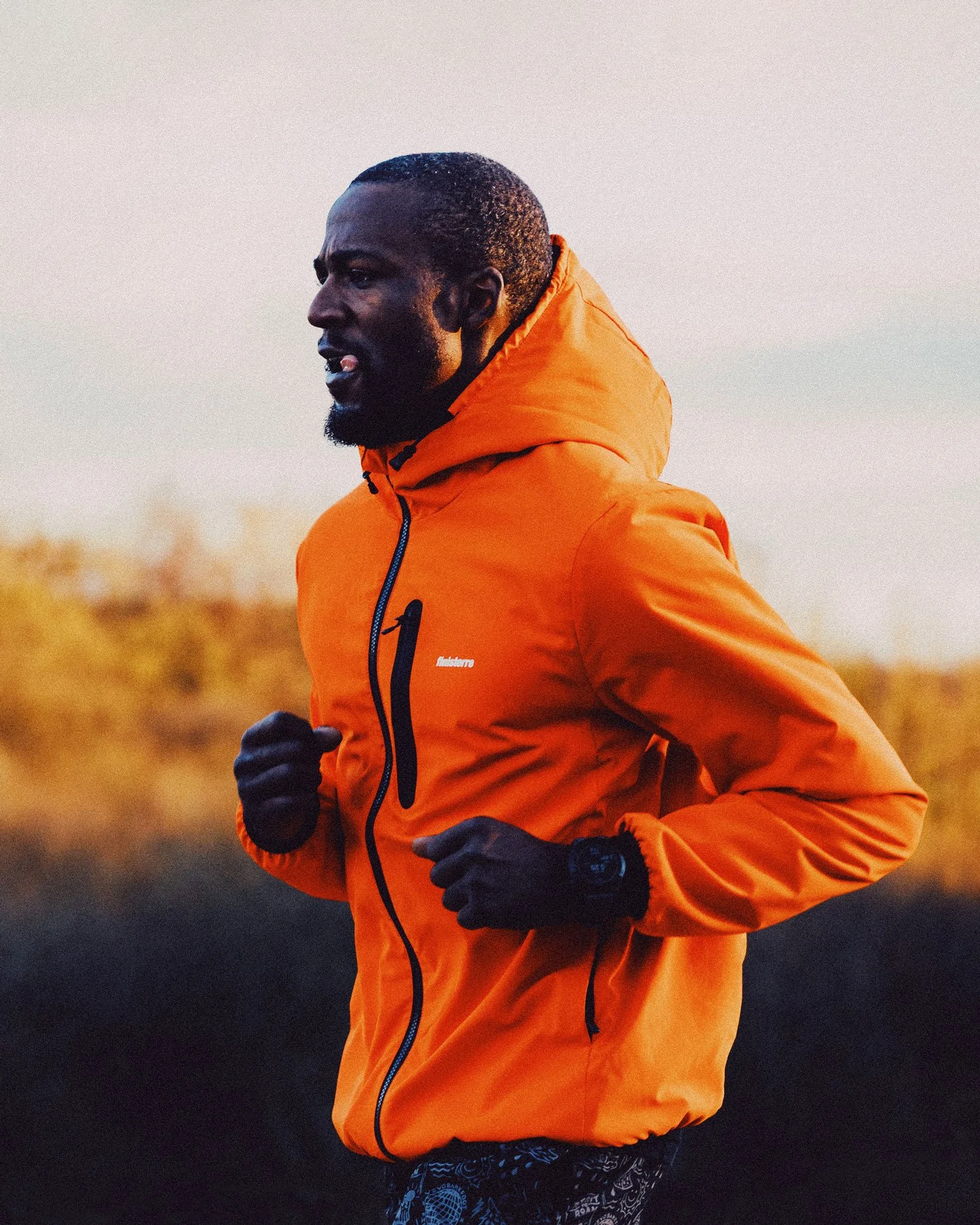 Lifestyle sports photograph of male runner in orange jacket at golden hour, outdoor brand campaign imagery