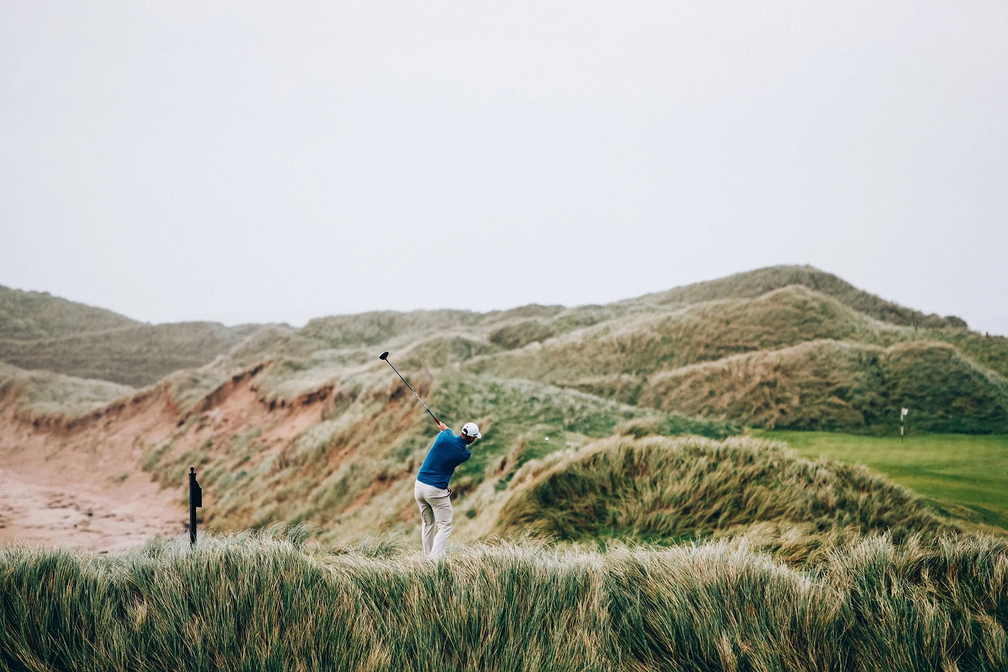 Golfer playing a shot through dramatic coastal dunes on a links golf course in Ireland