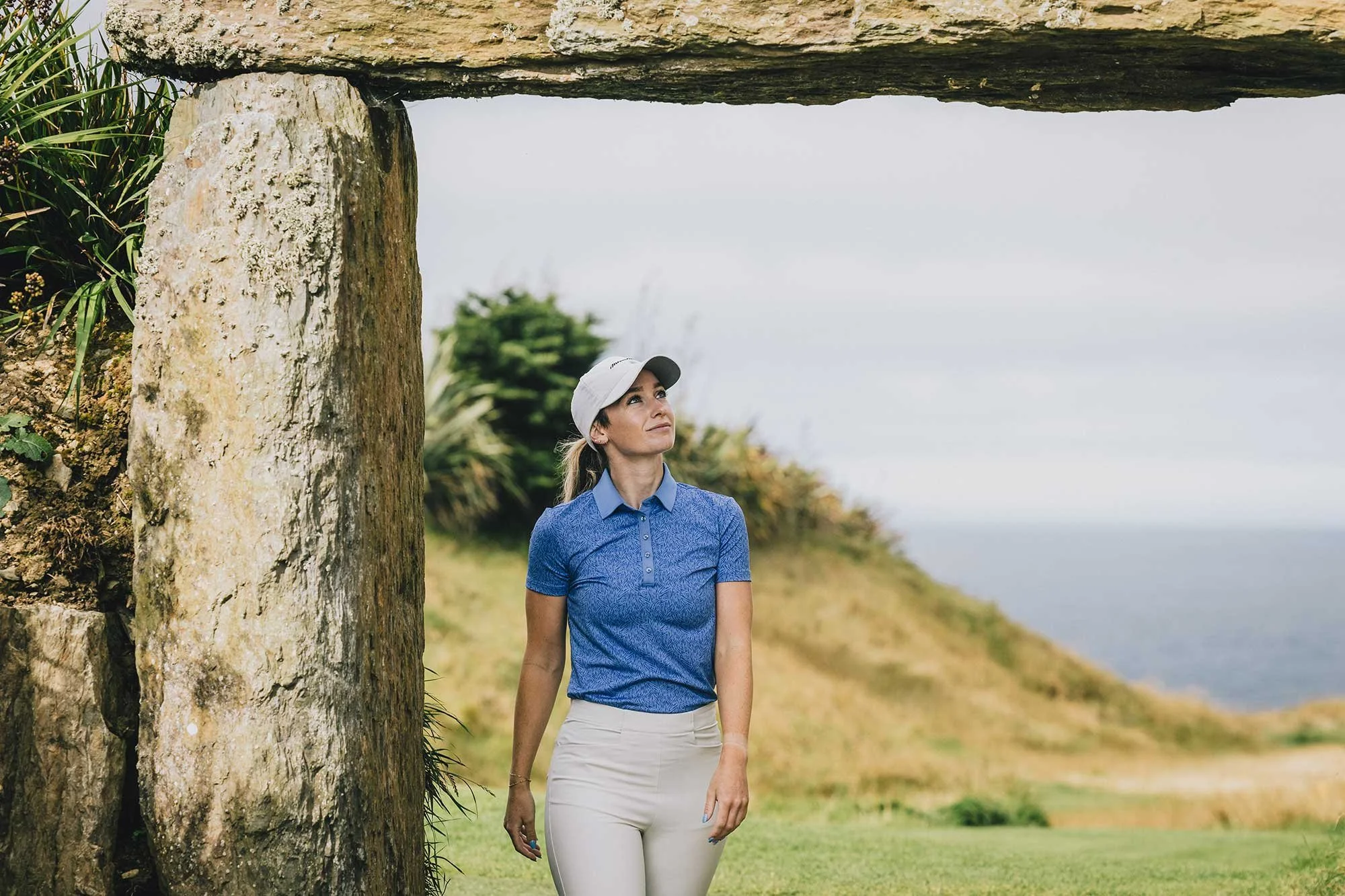 Female golfer beneath a stone arch overlooking the sea at Old Head Golf Links in Ireland