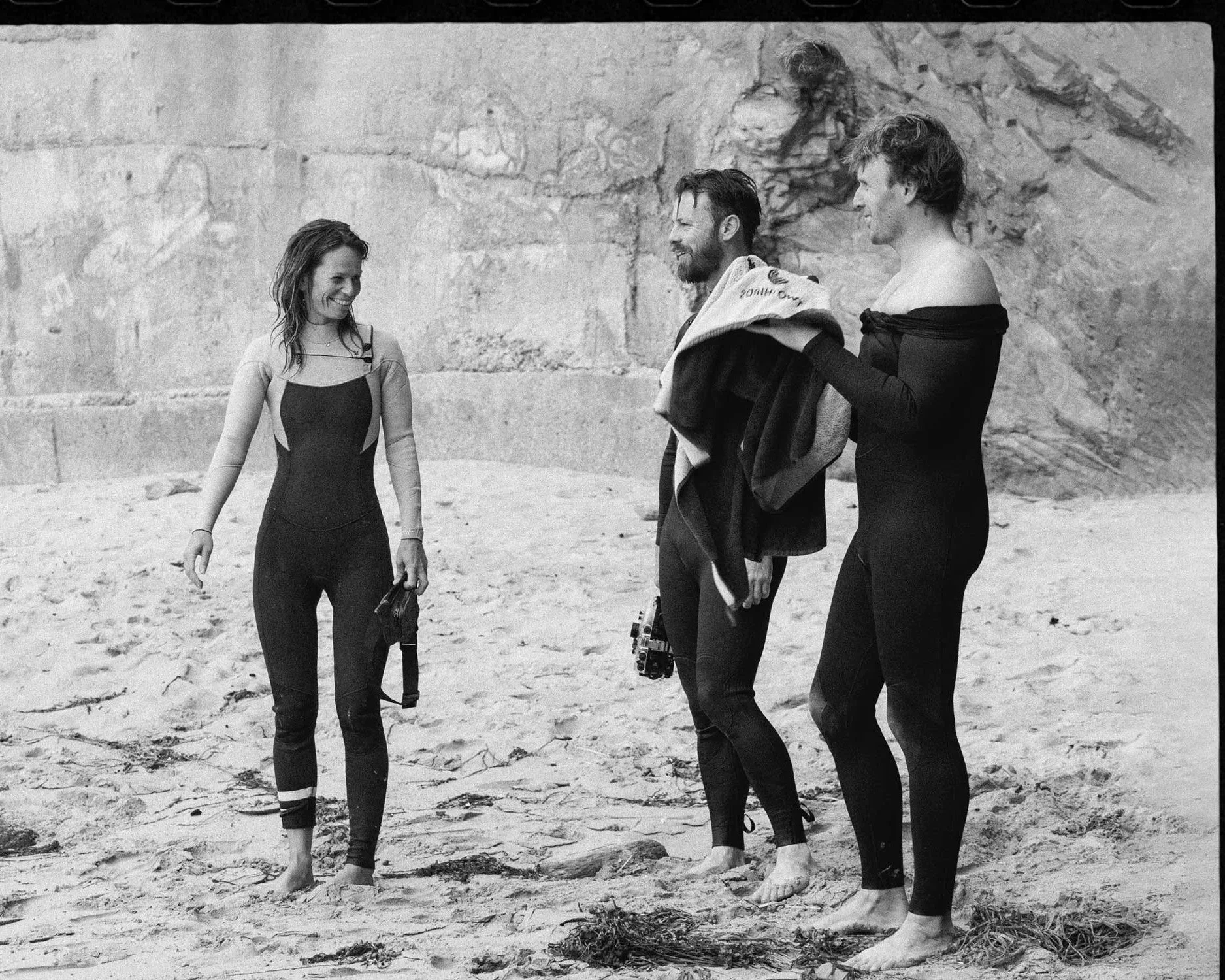 Black and white lifestyle photograph of surfers on sandy beach, editorial coastal brand photography