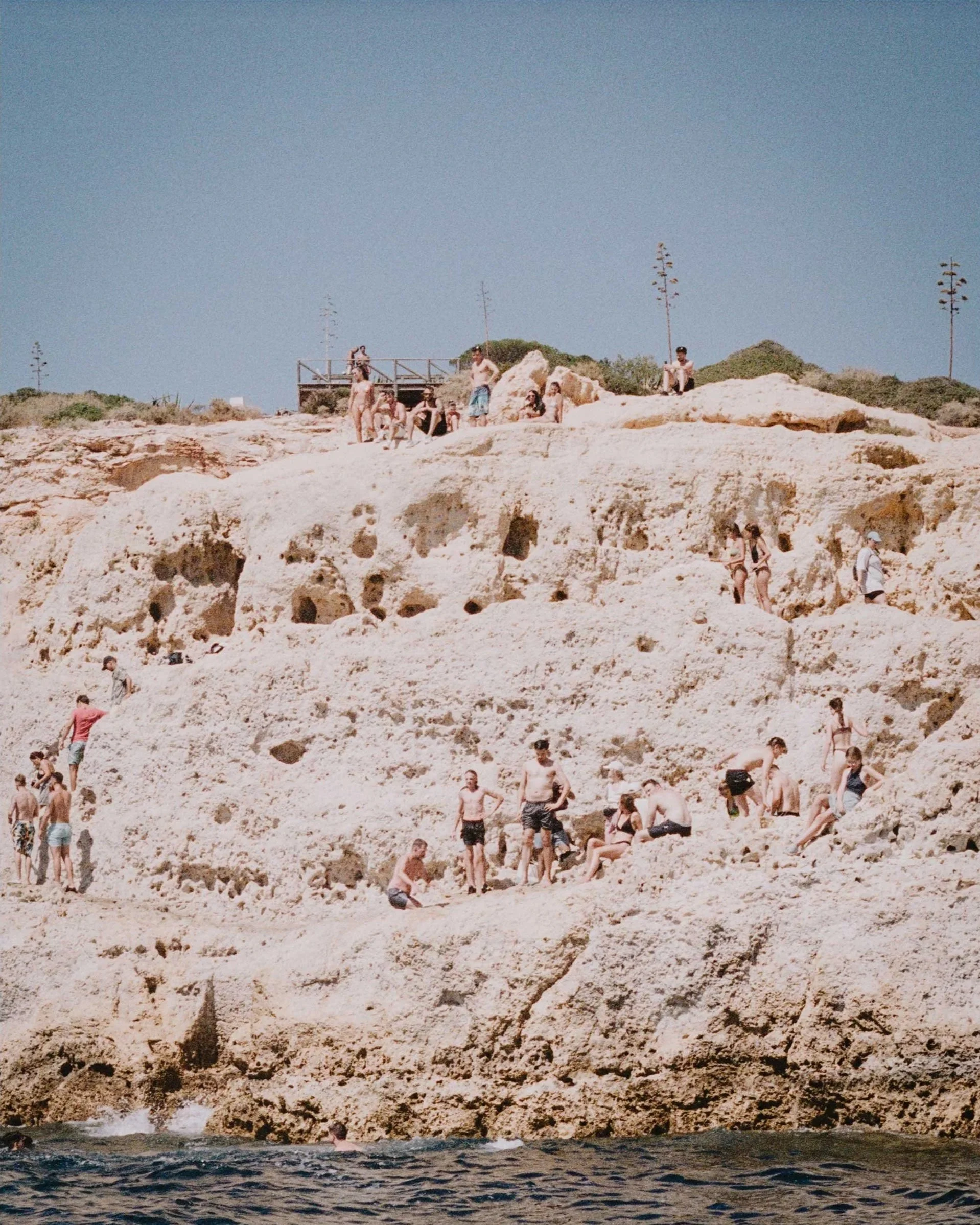 Coastal lifestyle photography, people gathered on rocky shoreline in natural light on film