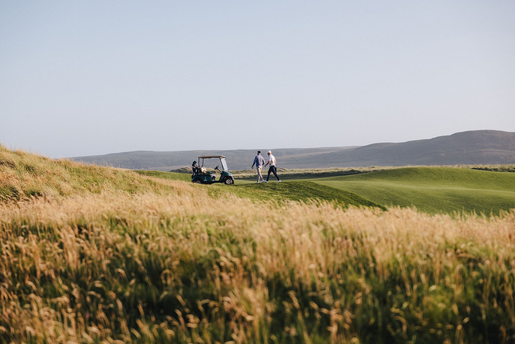 Golfers walking beside a golf cart through the rolling links landscape at The Machrie in Scotland