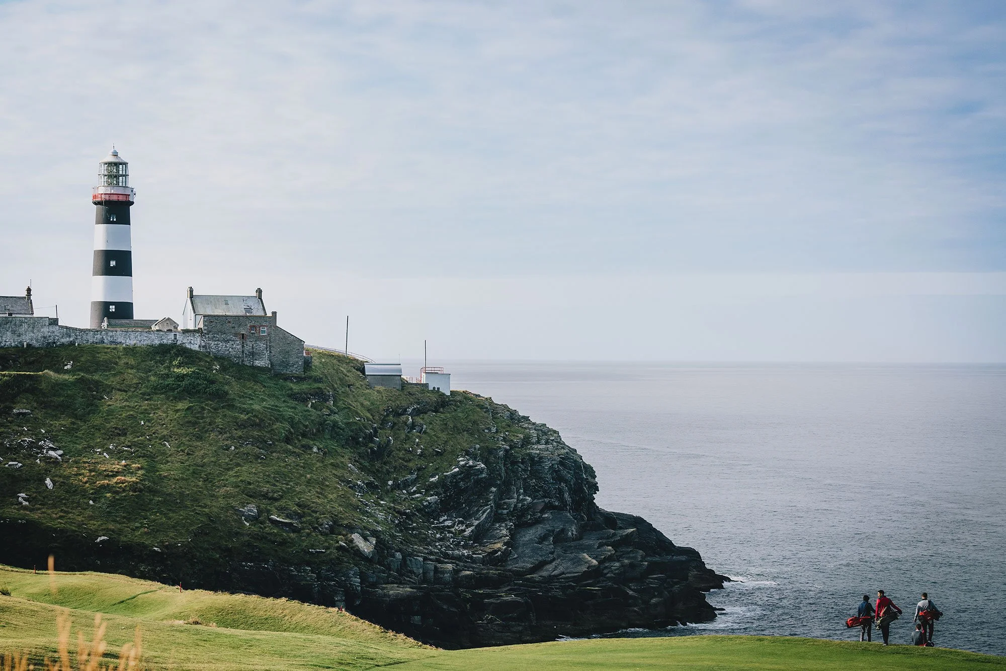 Golfers crossing a coastal fairway beneath the Old Head lighthouse