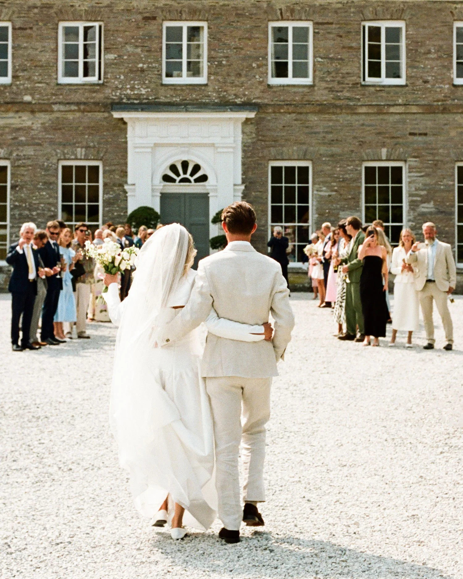 Documentary wedding photography on film, couple walking through guests outside Cornwall country house venue