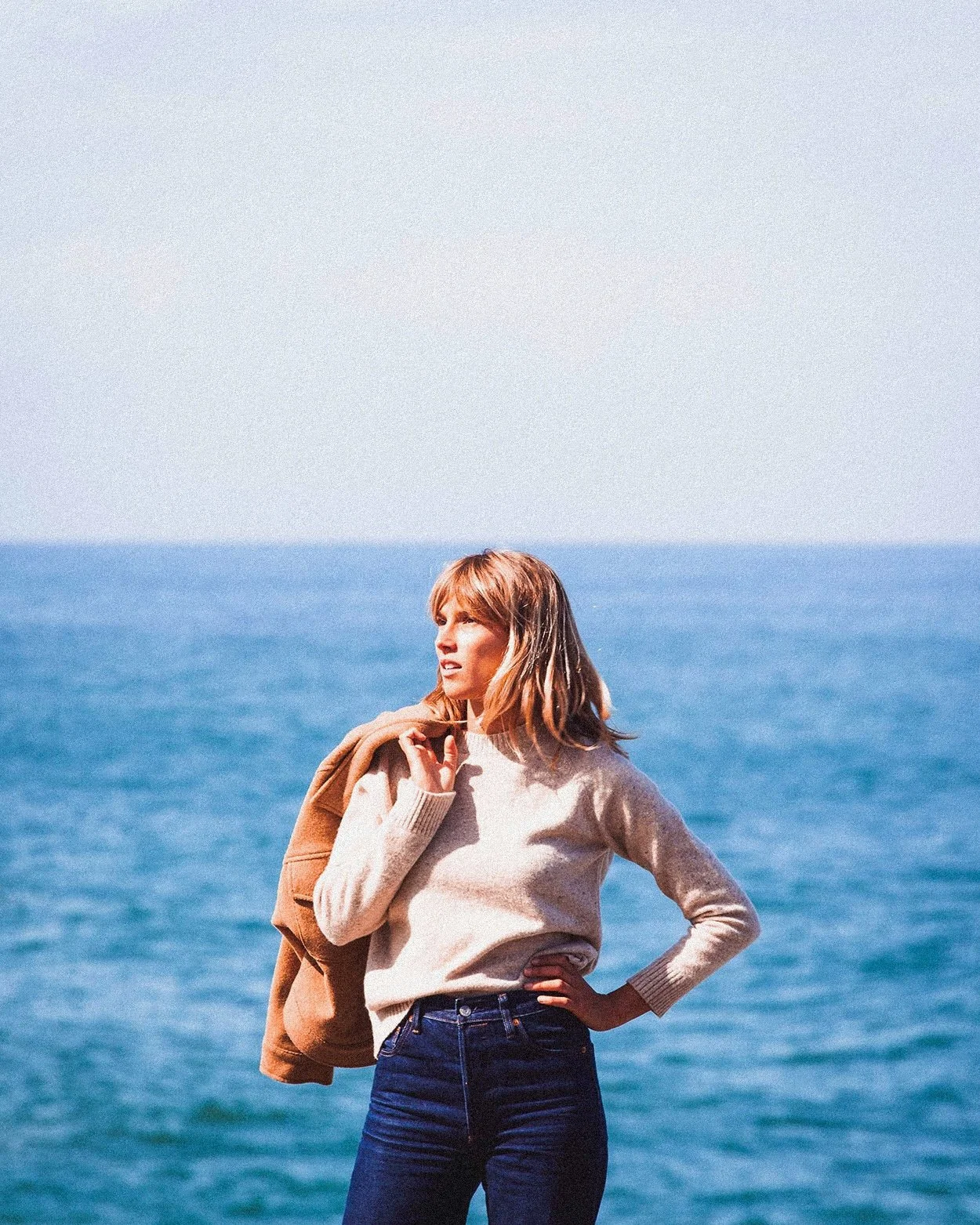 Lifestyle fashion photograph of woman standing by the sea, coastal editorial brand imagery