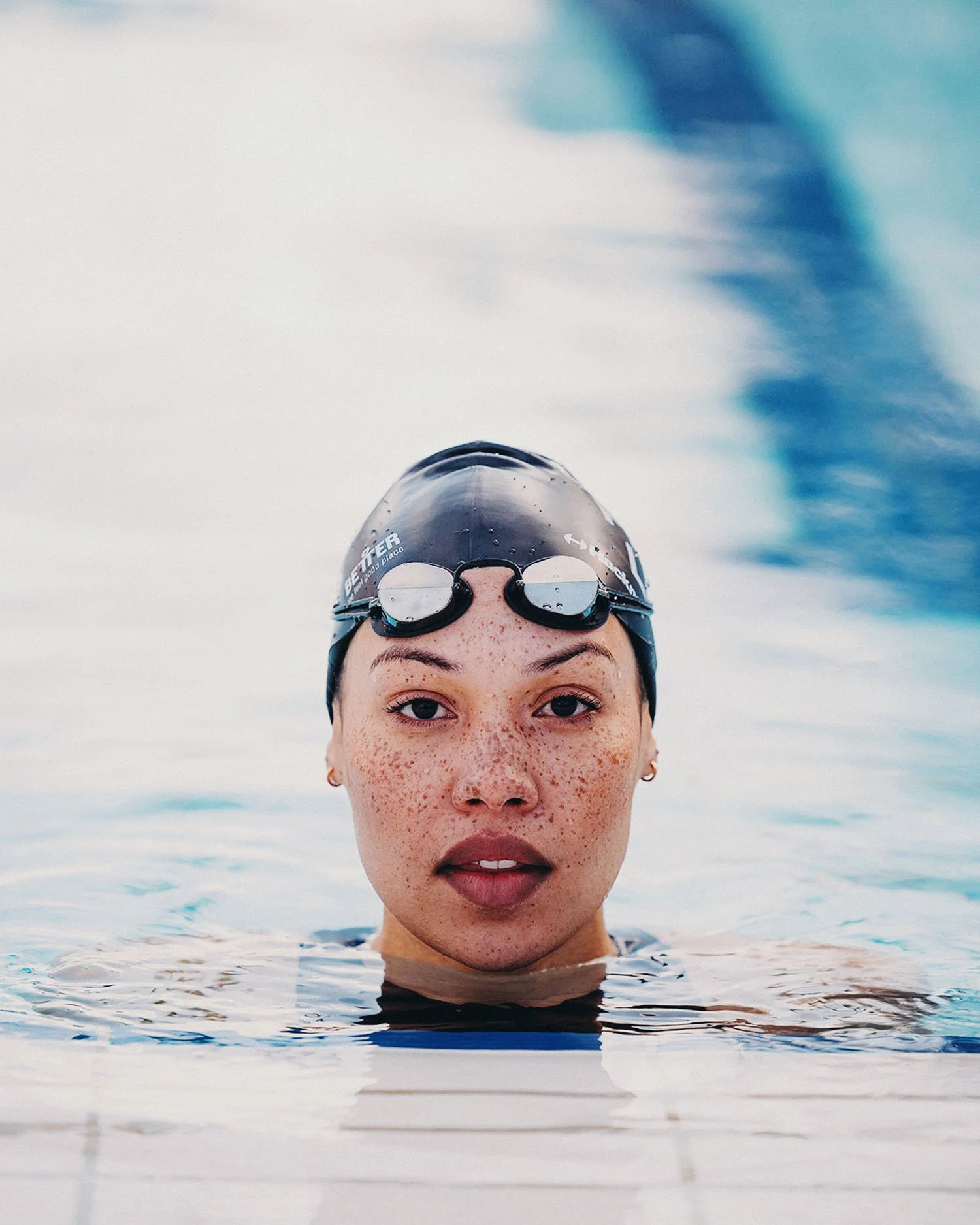 Lifestyle portrait of female swimmer in outdoor pool wearing goggles, editorial sports photography