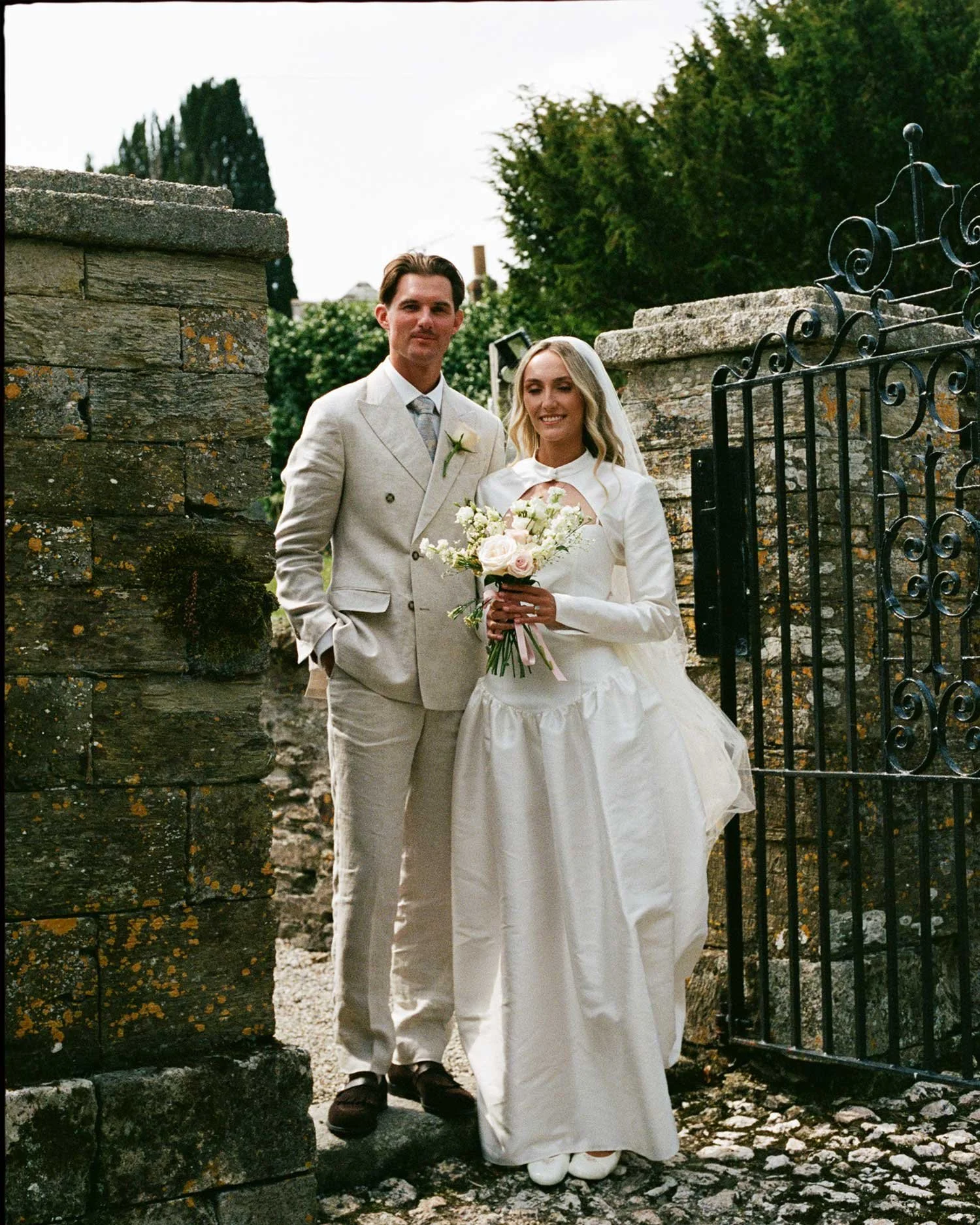 Editorial 35mm film wedding photograph of couple at stone gate, natural light portrait