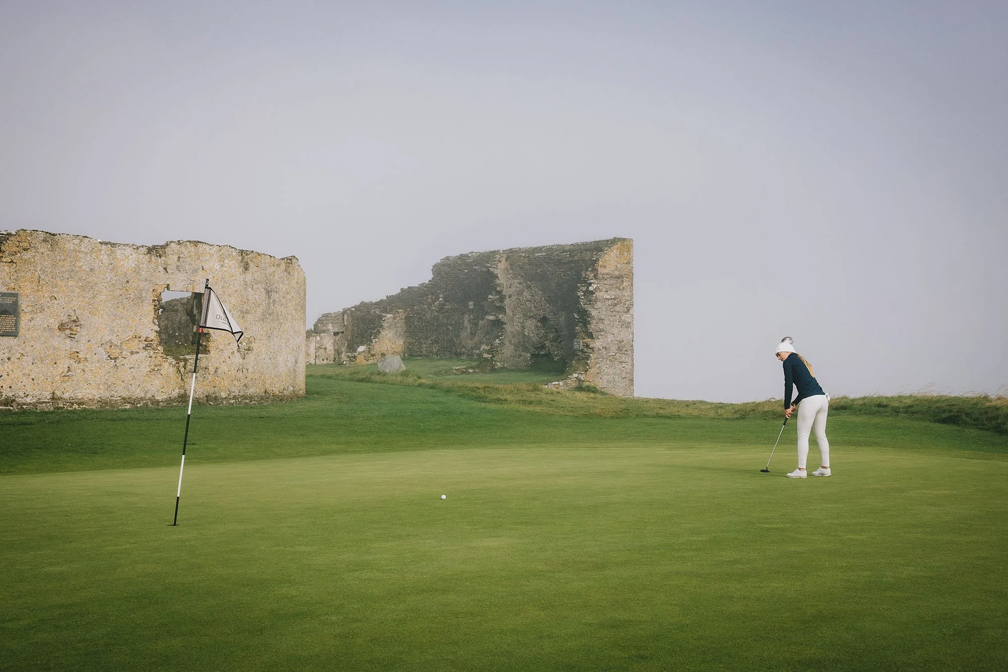 Golfer putting beside historic stone ruins at Old Head Ireland