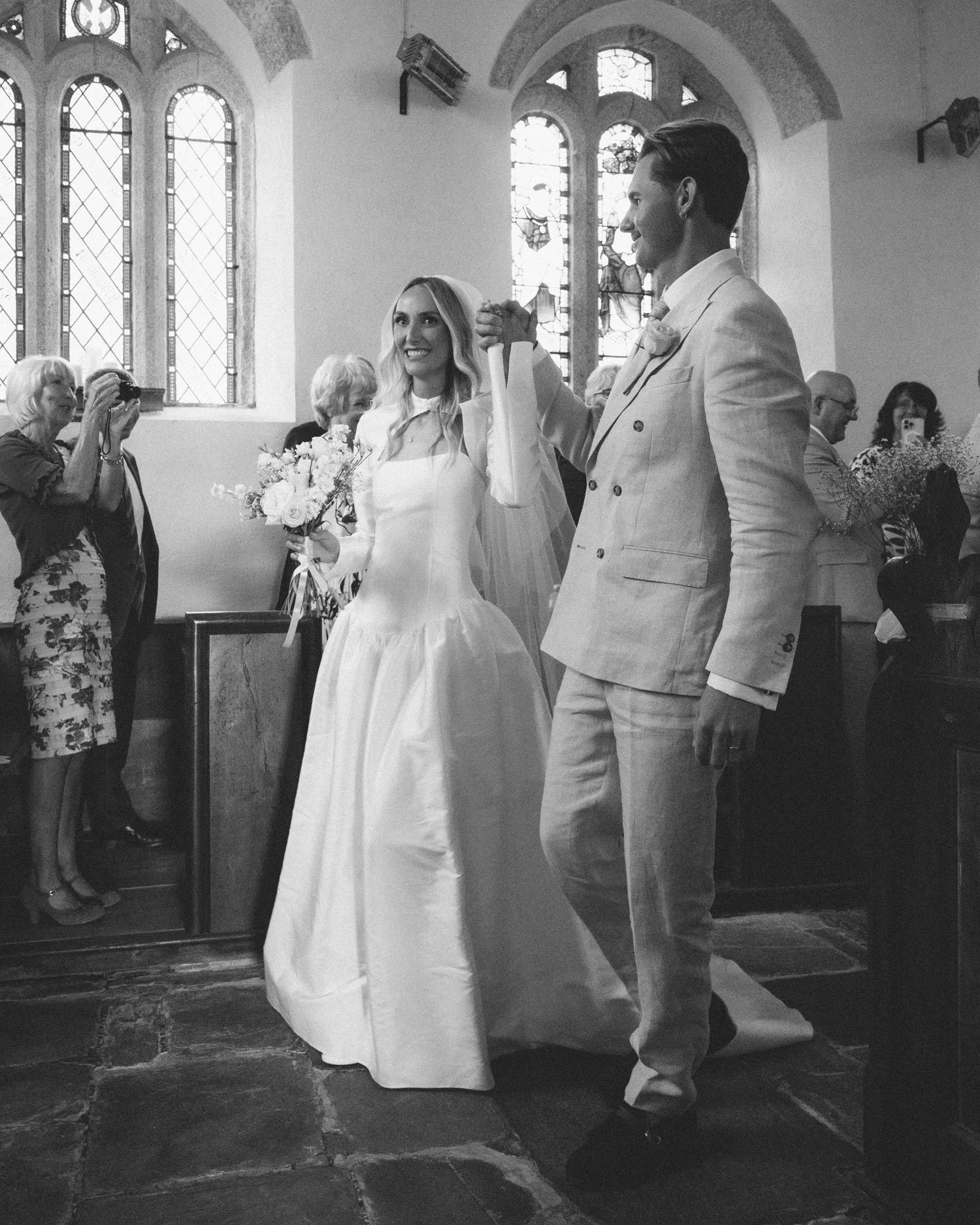 Black and white documentary wedding photograph on film, couple walking down church aisle after ceremony