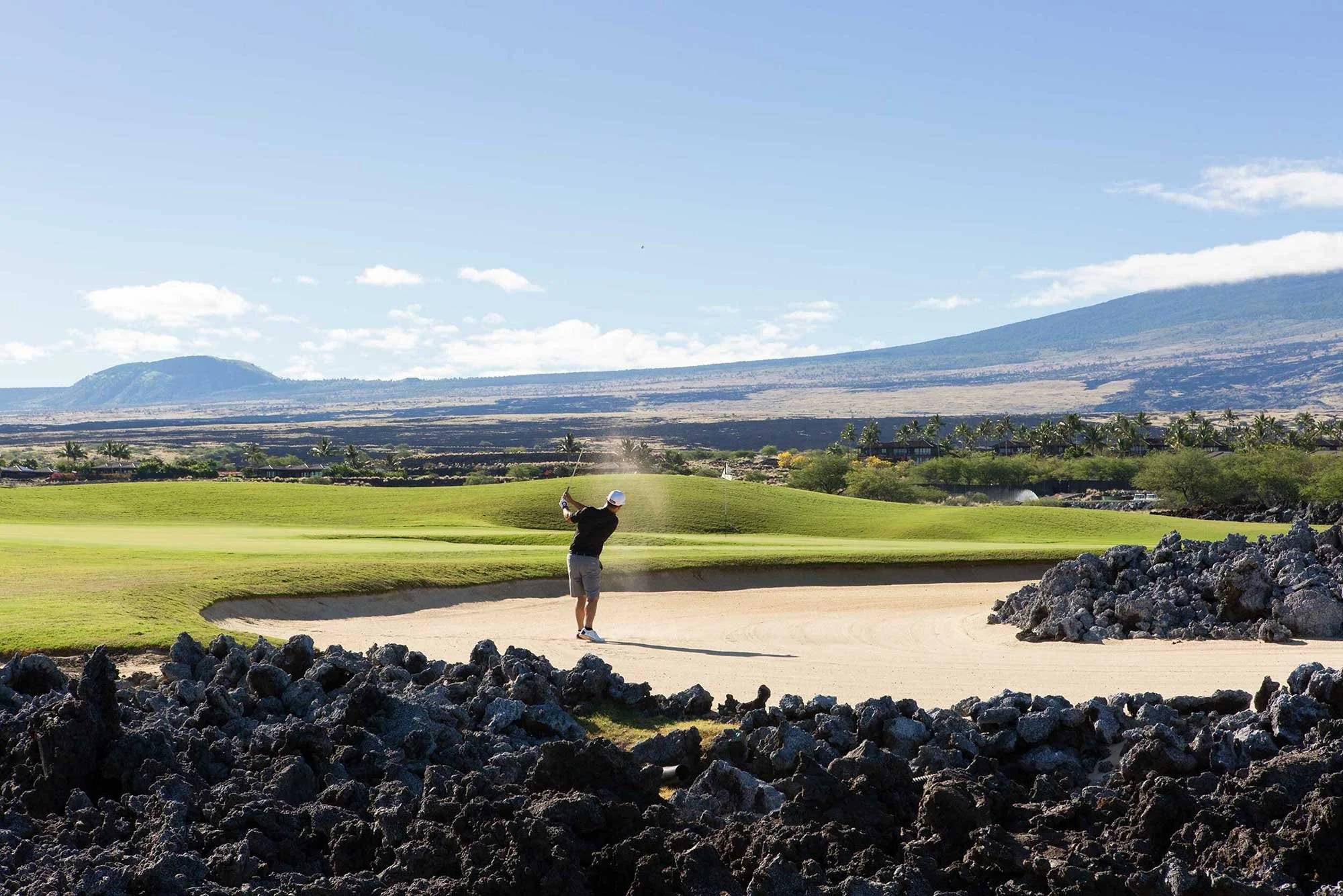 Golfer framed by volcanic rock with mountains beyond at Four Seasons Hawaii