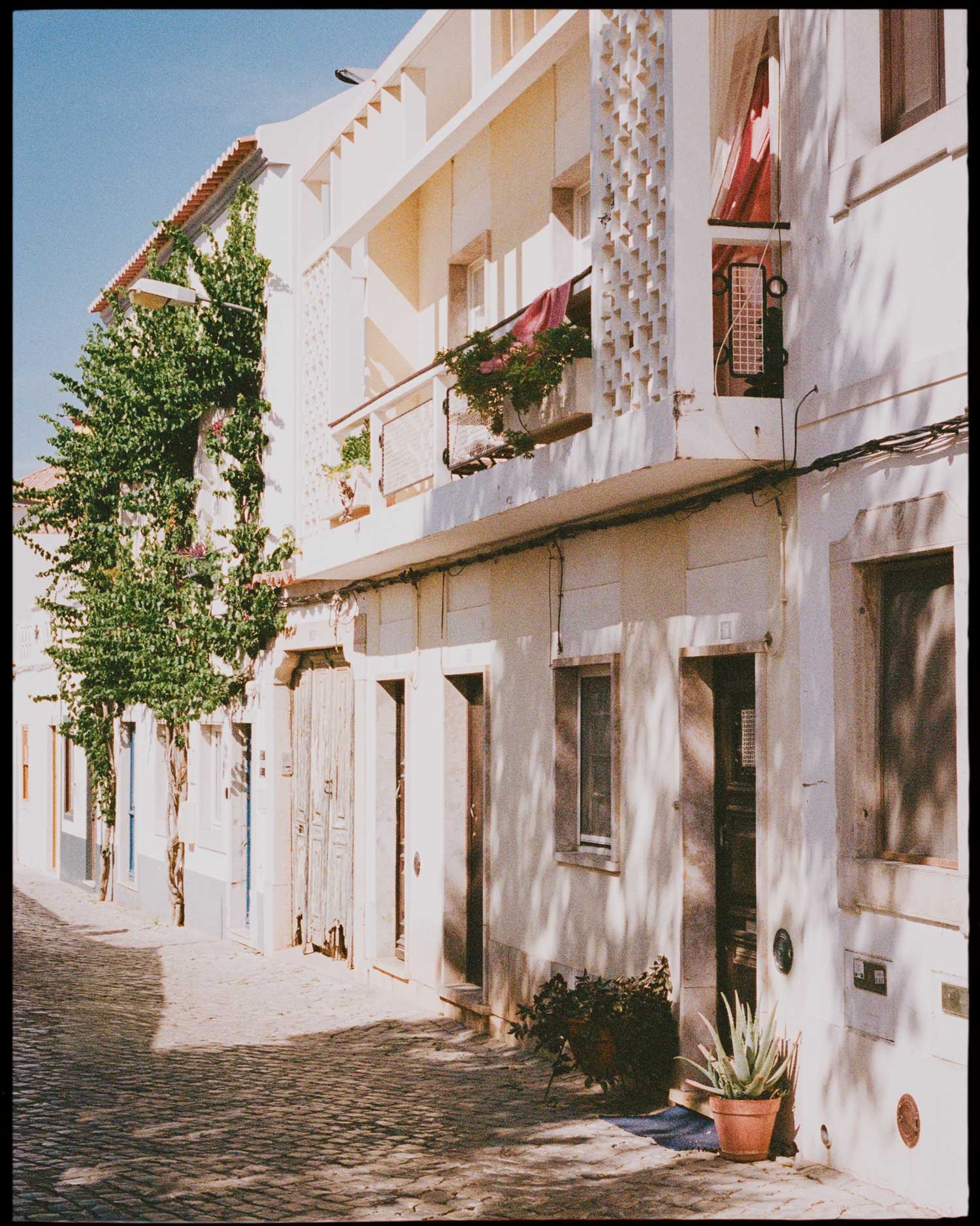 Editorial film photograph of sunlit Mediterranean street with pastel architecture, analogue travel work by Karl Mackie