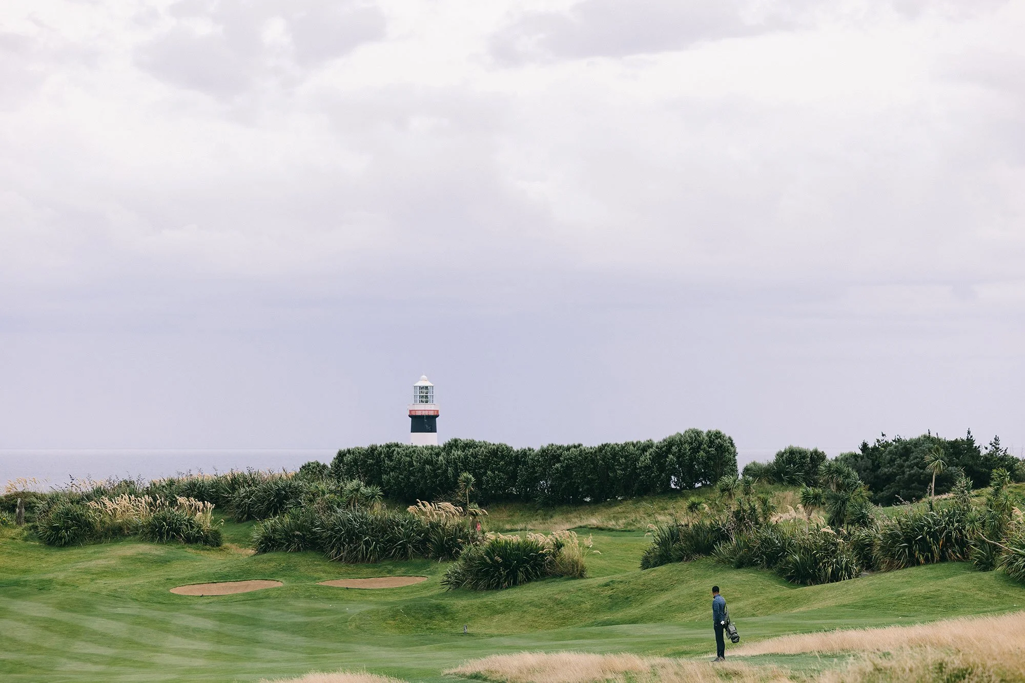 Golfer stood on the fairway at Old Head Golf Links in Ireland beneath the iconic black-and-white lighthouse
