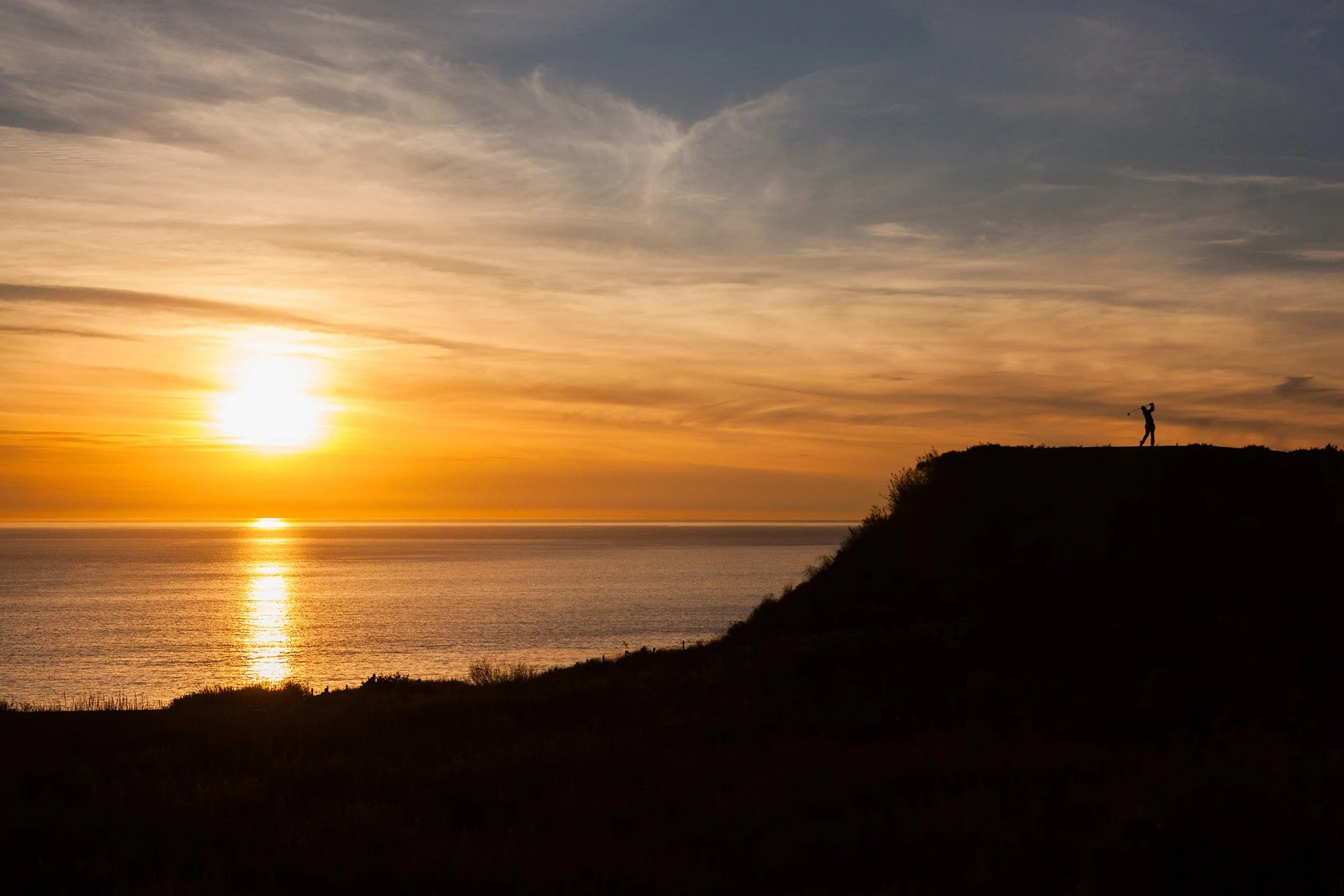 Silhouette of a golfer against a golden sunset over the Pacific Ocean in Los Angeles