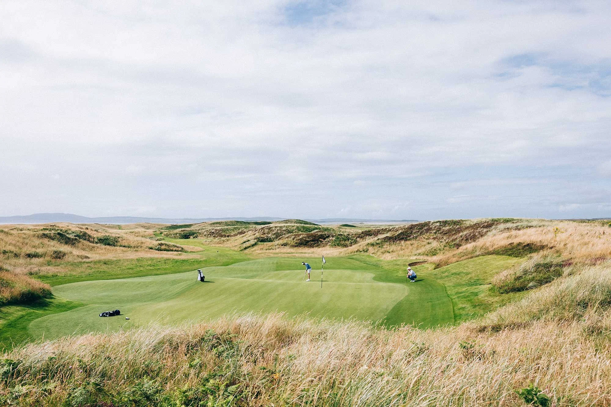 Golfers putting on a green surrounded by rolling links dunes at The Machrie in Scotland