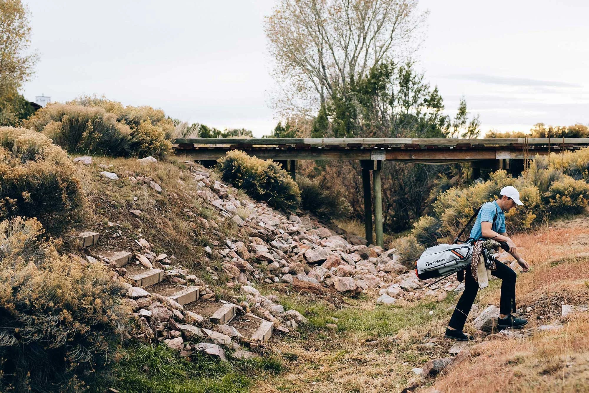 Golfer carrying clubs through rugged Arizona desert terrain