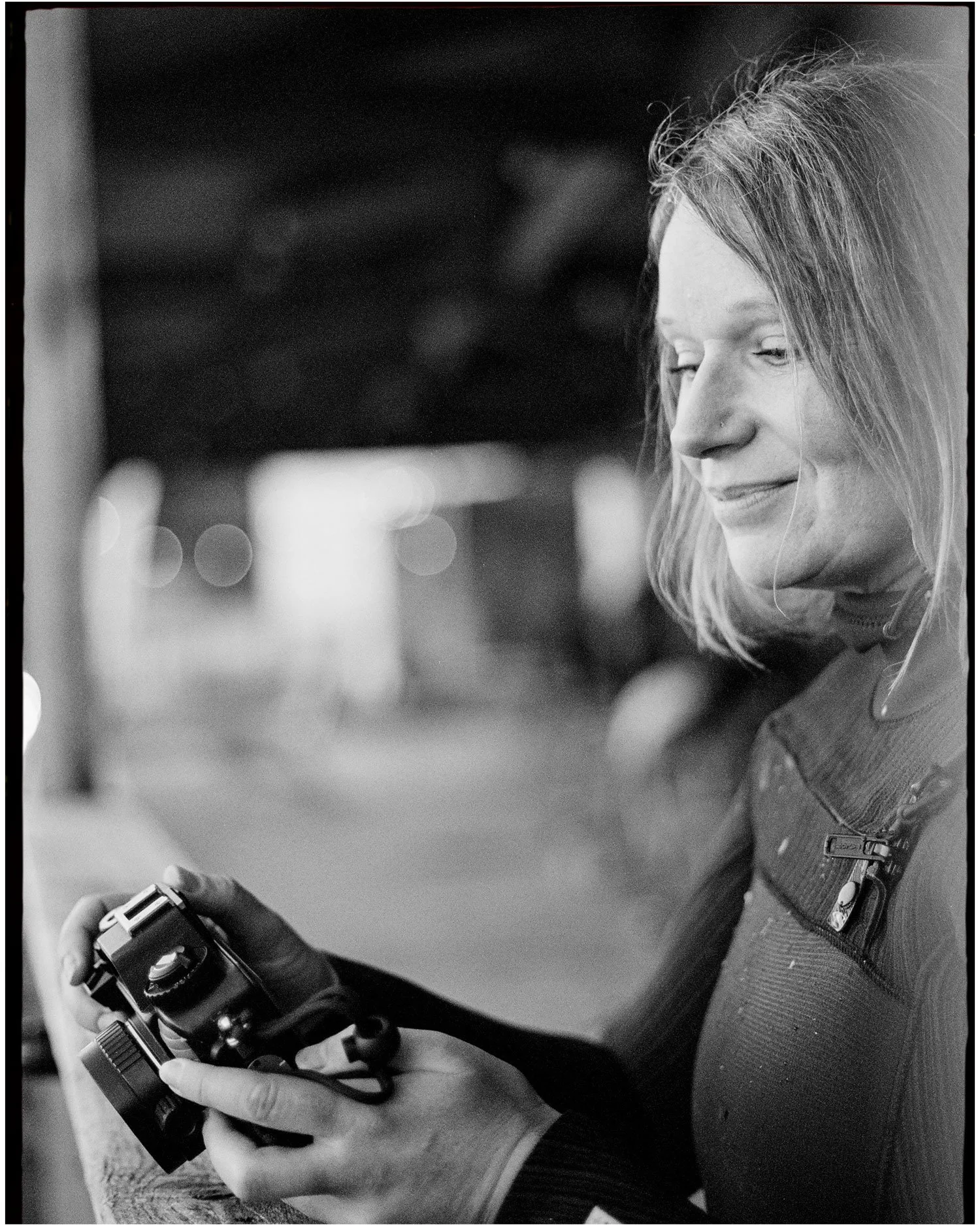 Black and white lifestyle portrait of woman holding camera, documentary style photography