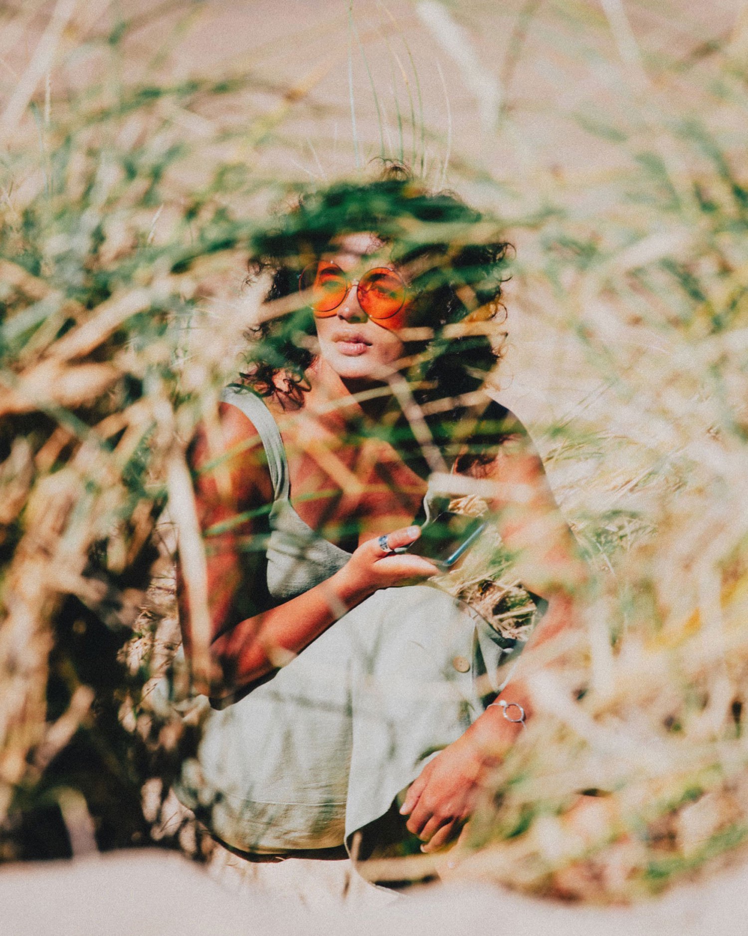 Editorial lifestyle portrait of woman in sunglasses surrounded by tall grass, natural light outdoor photography