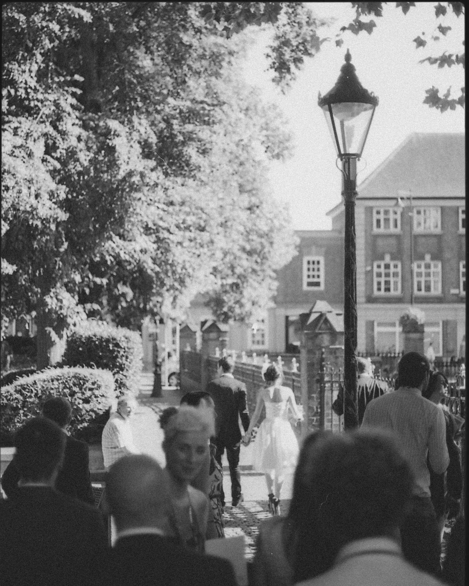 Black and white 35mm film photograph of a bride and groom walking through guests after their wedding ceremony in Leicester. Documentary wedding photography by Karl Mackie.