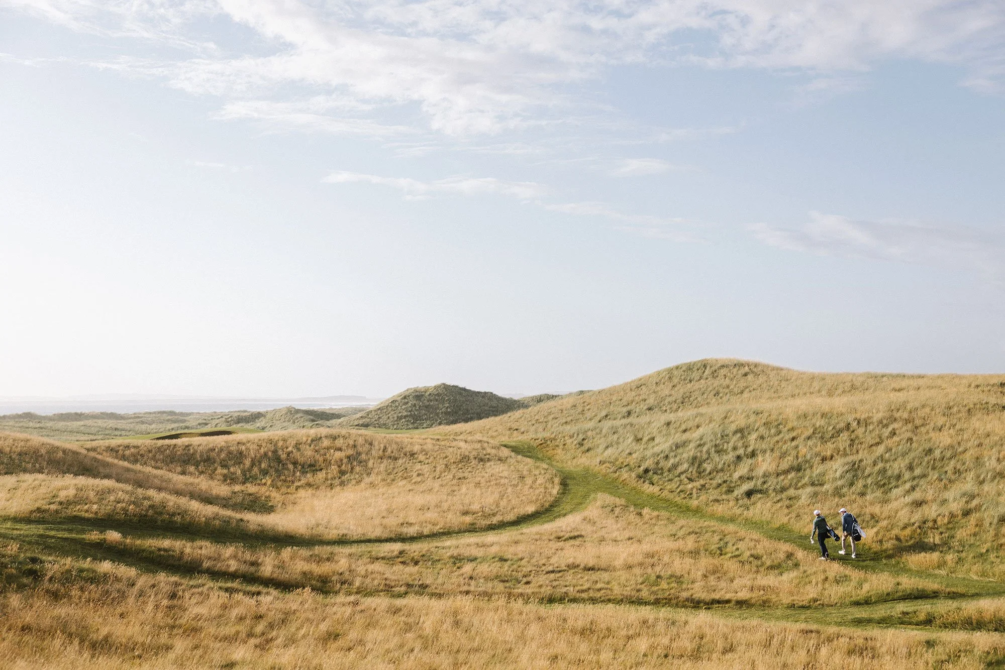 Golfers walking through sweeping links dunes