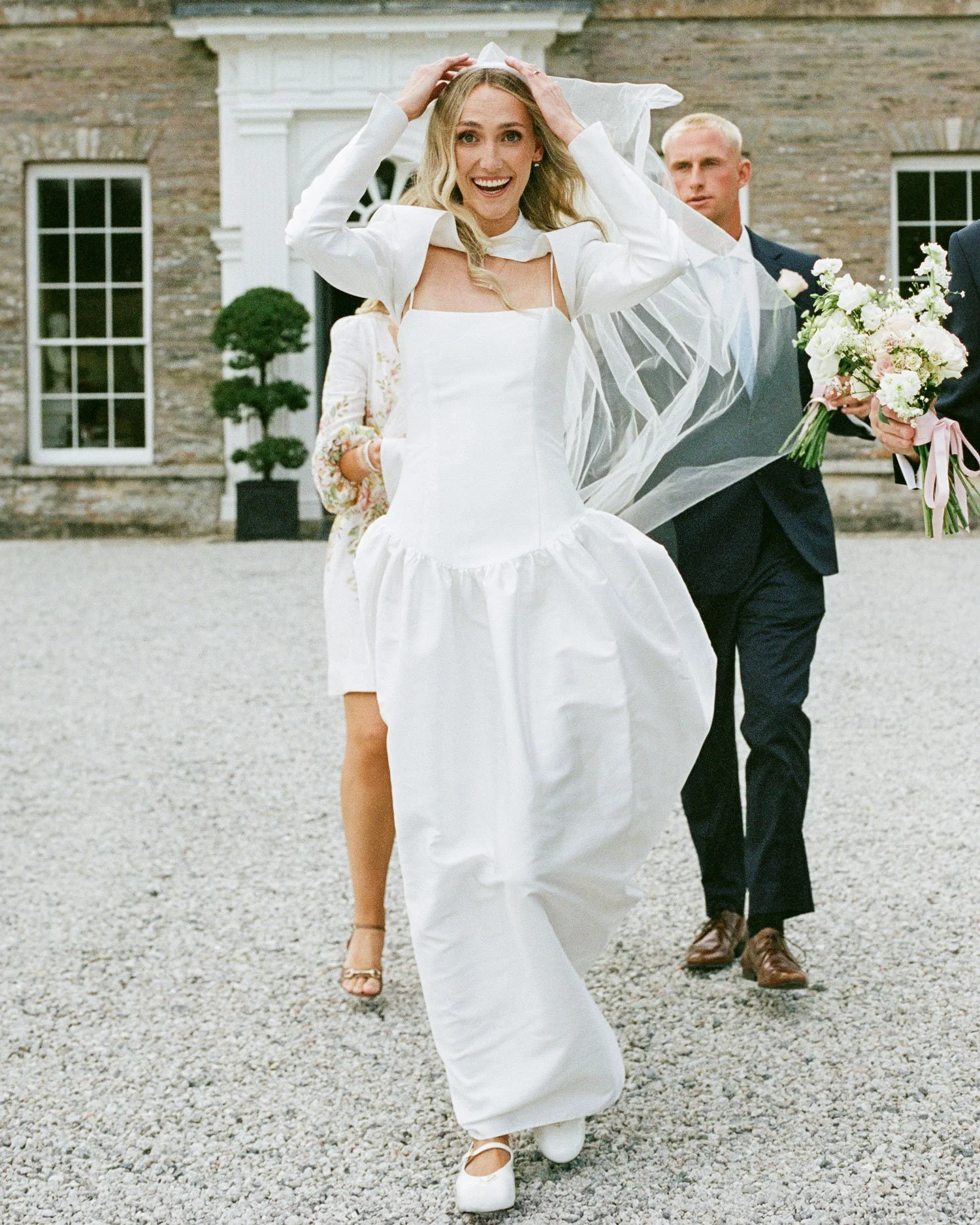 Film documentary wedding photograph of bride walking through courtyard, candid natural light moment captured on 35mm
