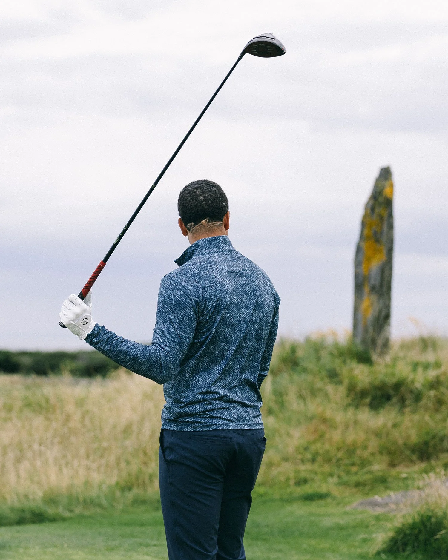 Golfer holding a club beside a standing stone at Old Head Golf Links